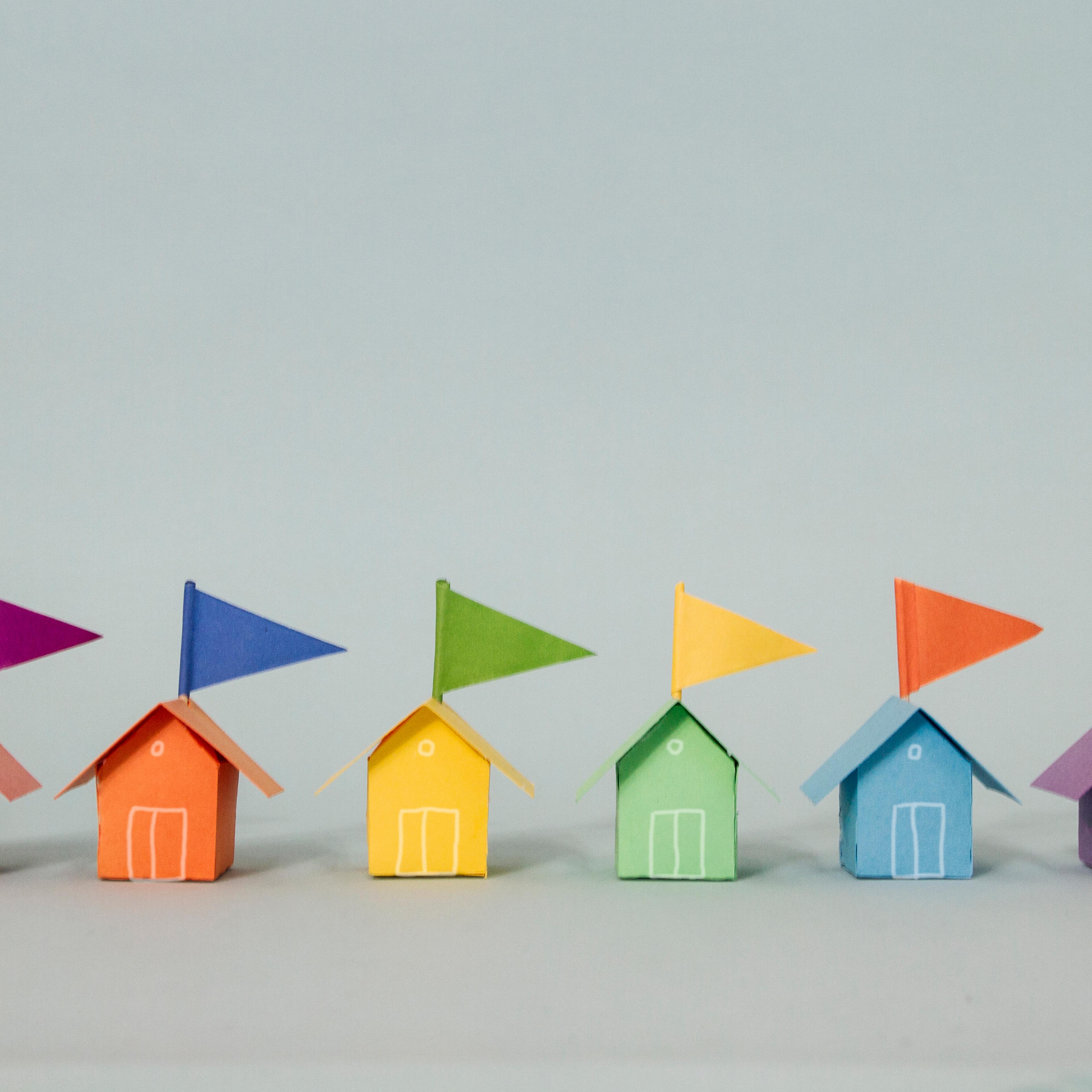 A row of rainbow coloured beach huts complete with contrasting paper flags made out of paper