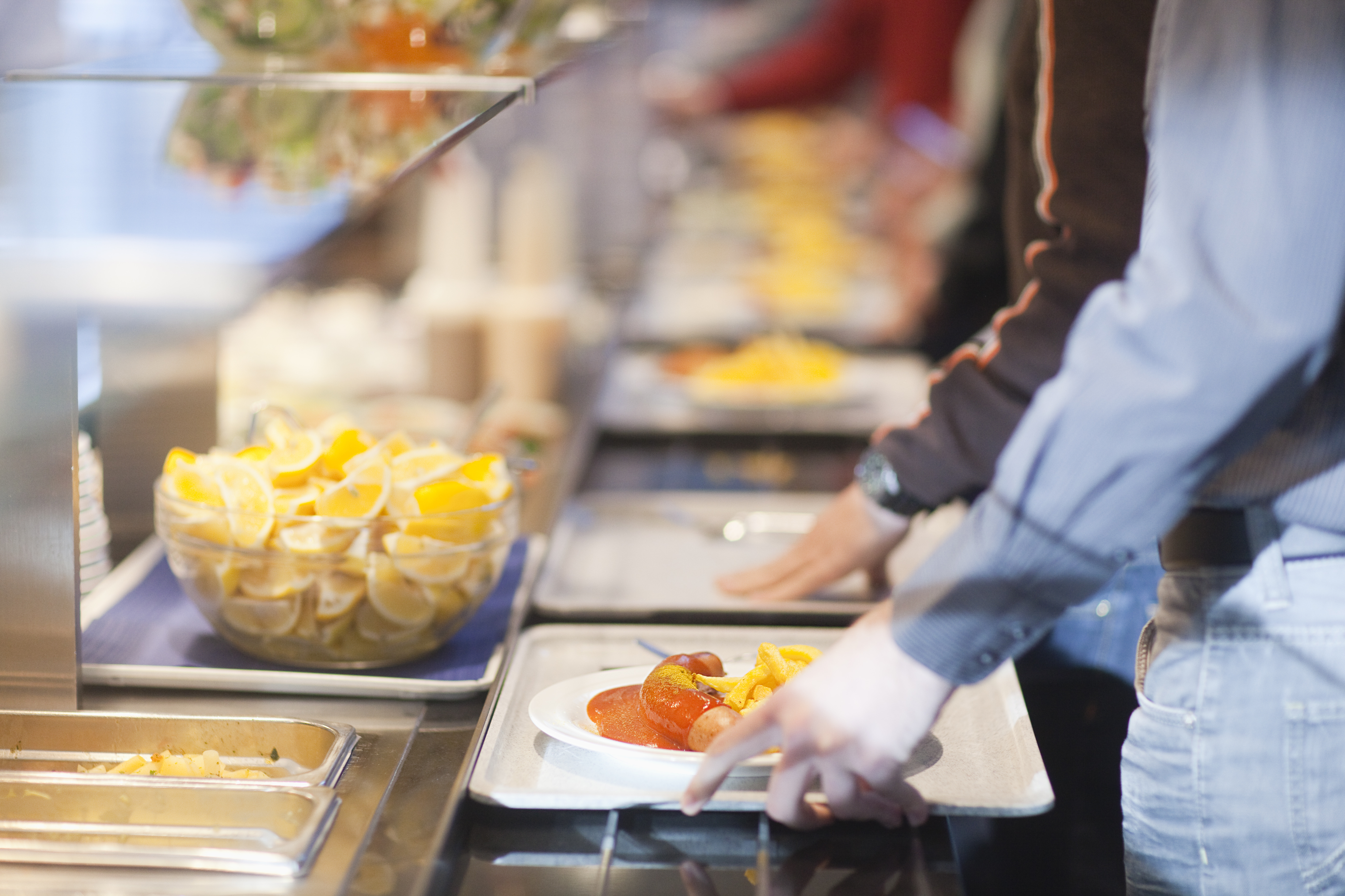 Close-up of men in line with food trays in work cafeteria