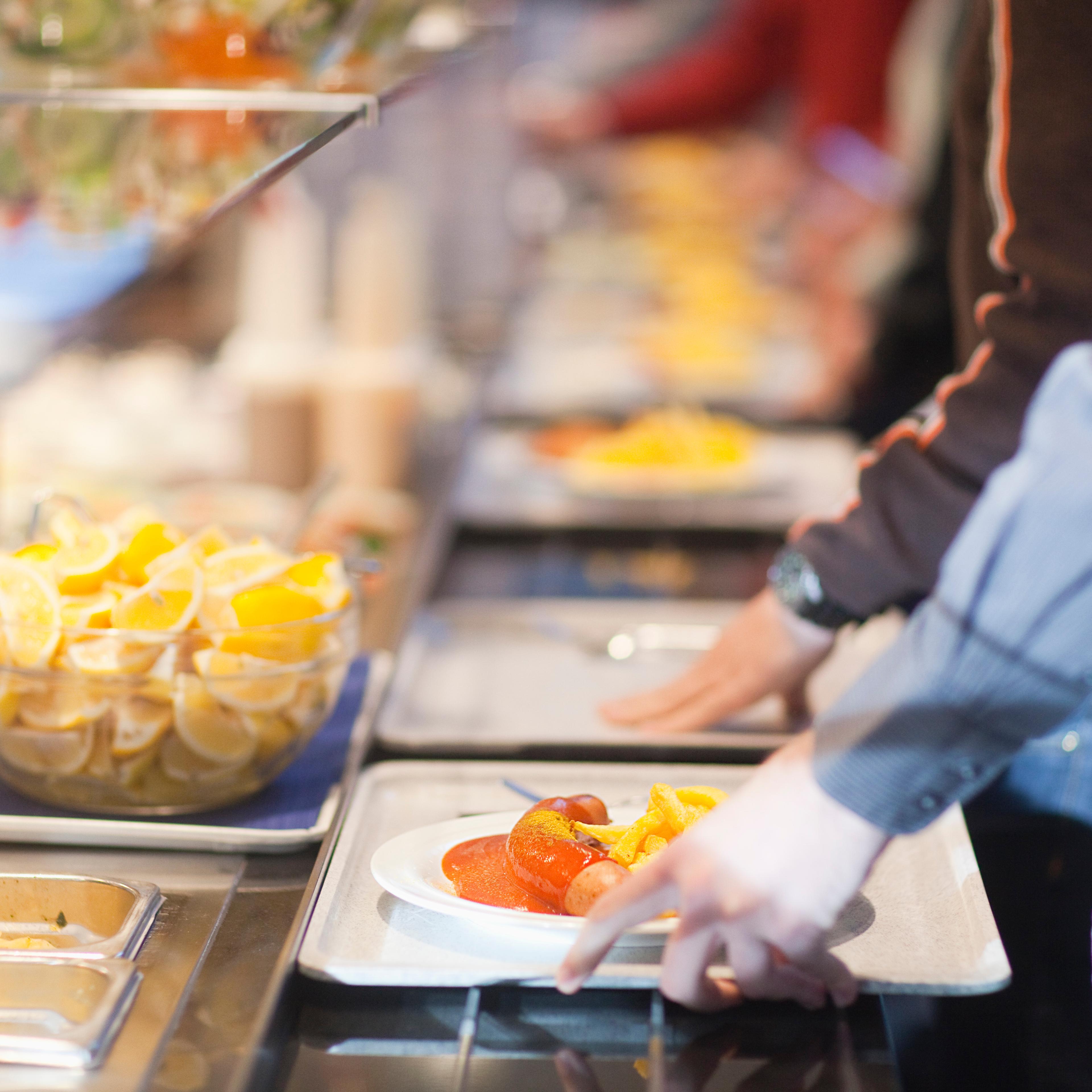 Close-up of men in line with food trays in work cafeteria