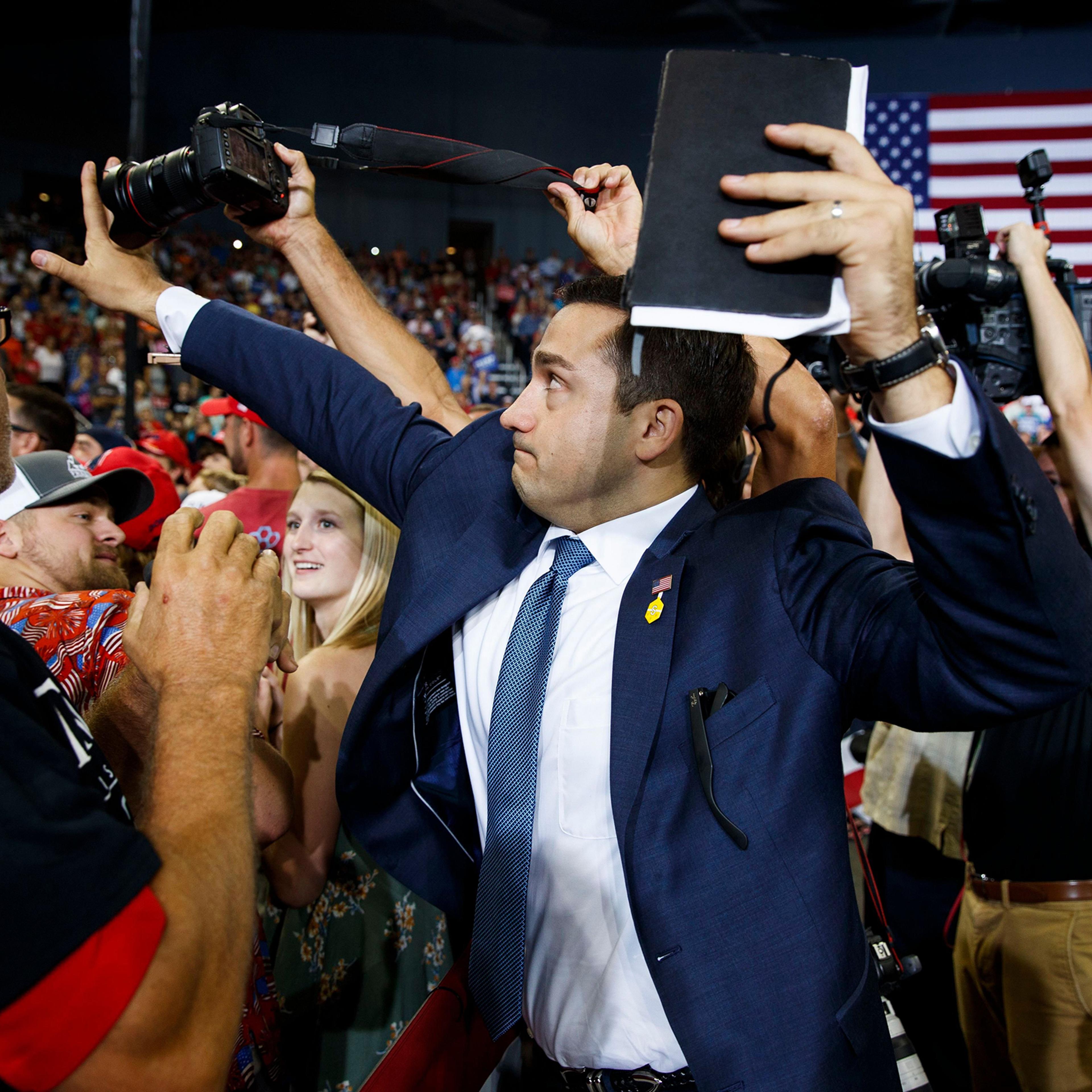 A staff member for President Donald Trump blocks a camera as a photojournalist attempts to take a photo of a protester during a campaign rally at the Ford Center, in Evansville, Ind, August 30, 2018.