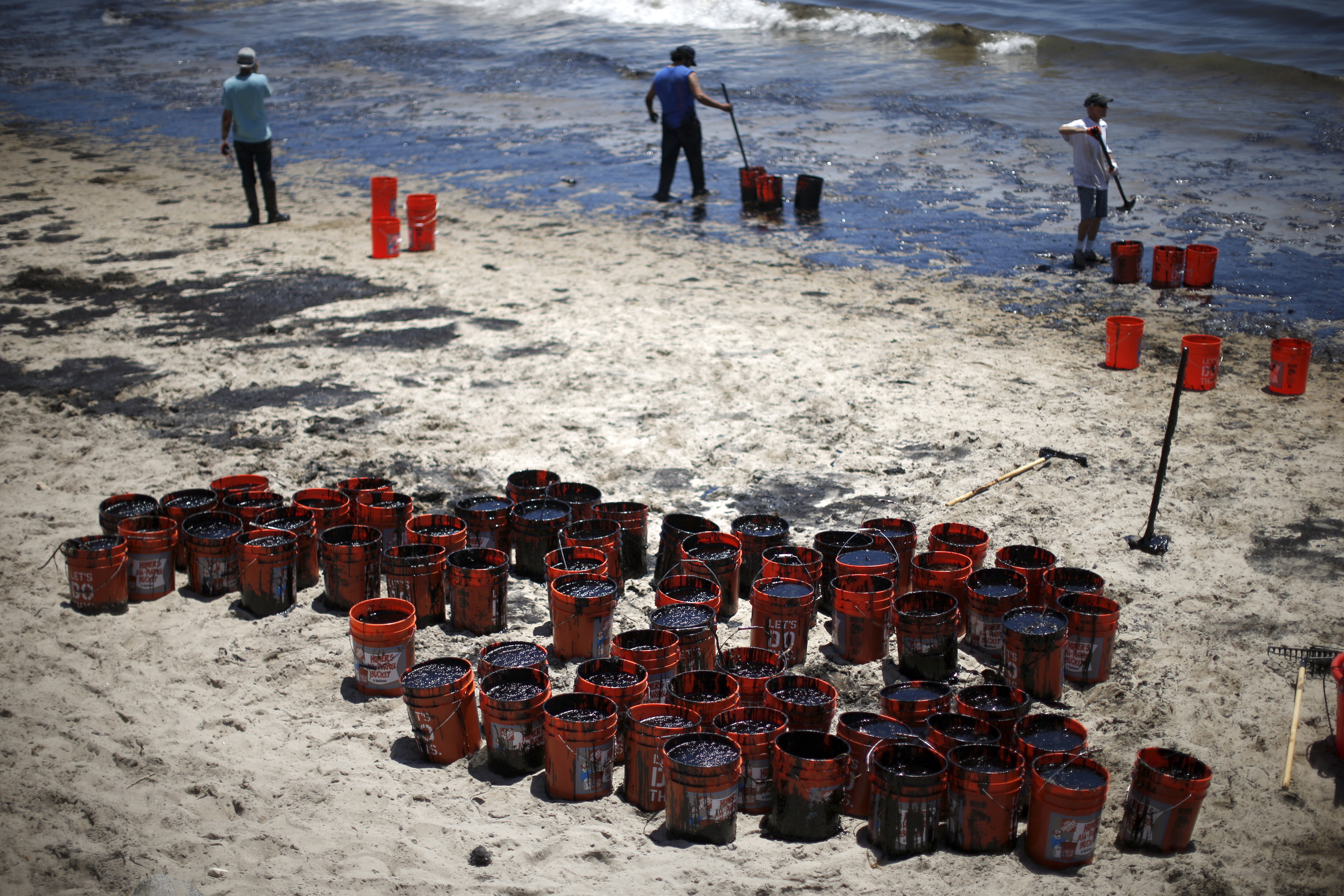 Volunteers fill buckets with oil from an oil slick along the coast of Refugio State Beach in Goleta