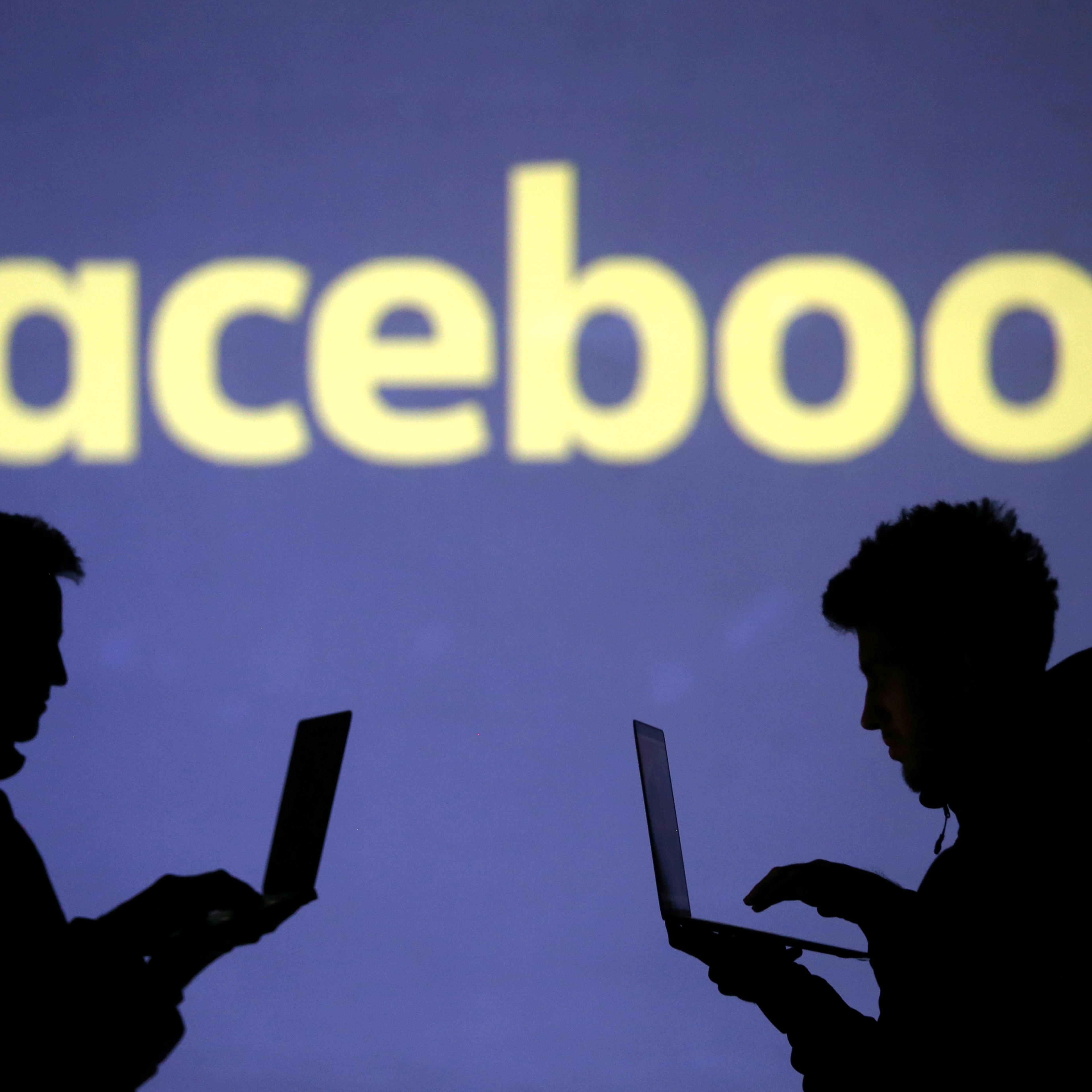 Silhouettes of laptop users are seen next to a screen projection of Facebook logo in this picture illustration