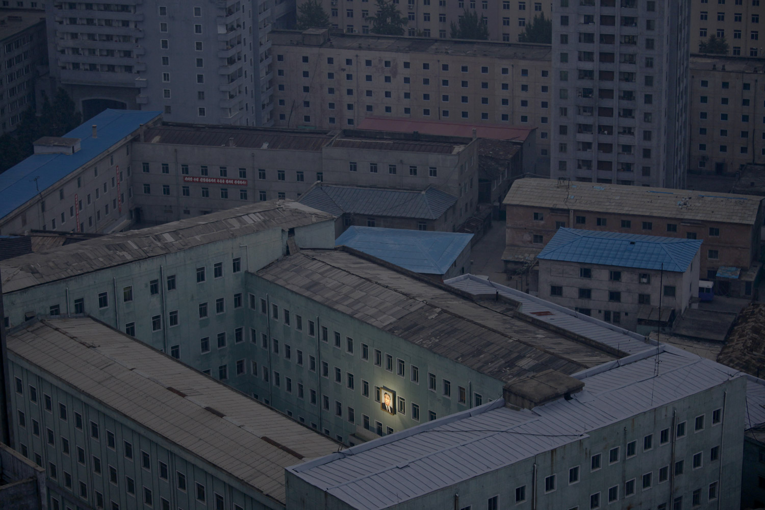 October 5, 2011. A portrait of Kim Il Sung, founder of the communist regime in North Korea, beams from a government building at 6 a.m. in the pariah state’s capital, Pyongyang. Soon the entire city would be awakened by propaganda songs blaring from the loudspeakers. 
