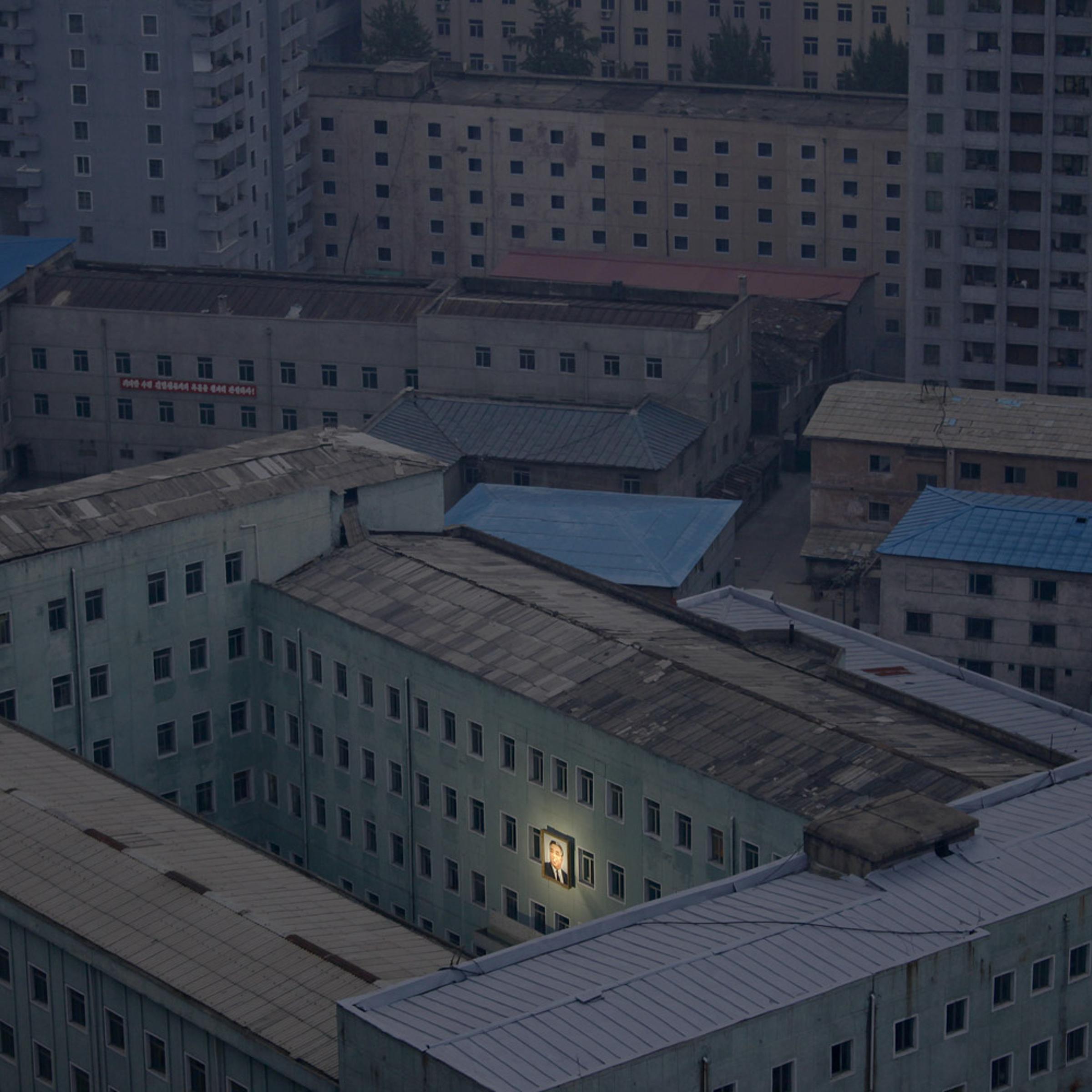October 5, 2011. A portrait of Kim Il Sung, founder of the communist regime in North Korea, beams from a government building at 6 a.m. in the pariah state’s capital, Pyongyang. Soon the entire city would be awakened by propaganda songs blaring from the loudspeakers.