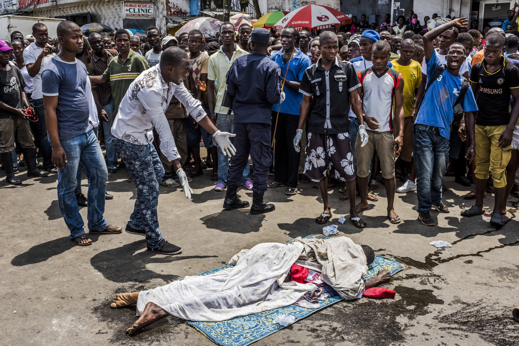 Residents look on as the body of a man suspected of dying from Ebola lies in a busy street, after it was reportedly dragged there to draw attention of burial teams following days of failed attempts by his family to have his body picked up, in Monrovia, L