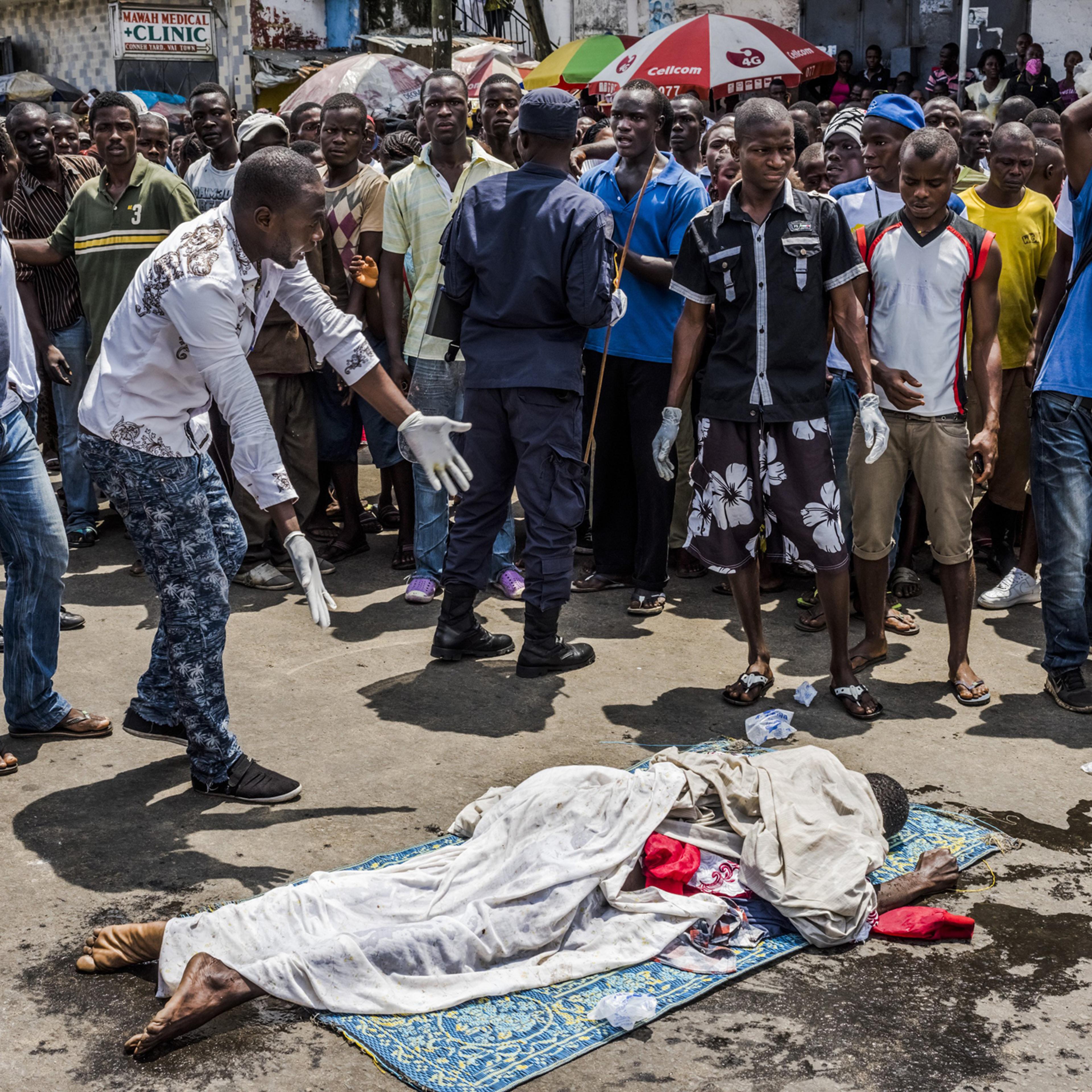 Residents look on as the body of a man suspected of dying from Ebola lies in a busy street, after it was reportedly dragged there to draw attention of burial teams following days of failed attempts by his family to have his body picked up, in Monrovia, L