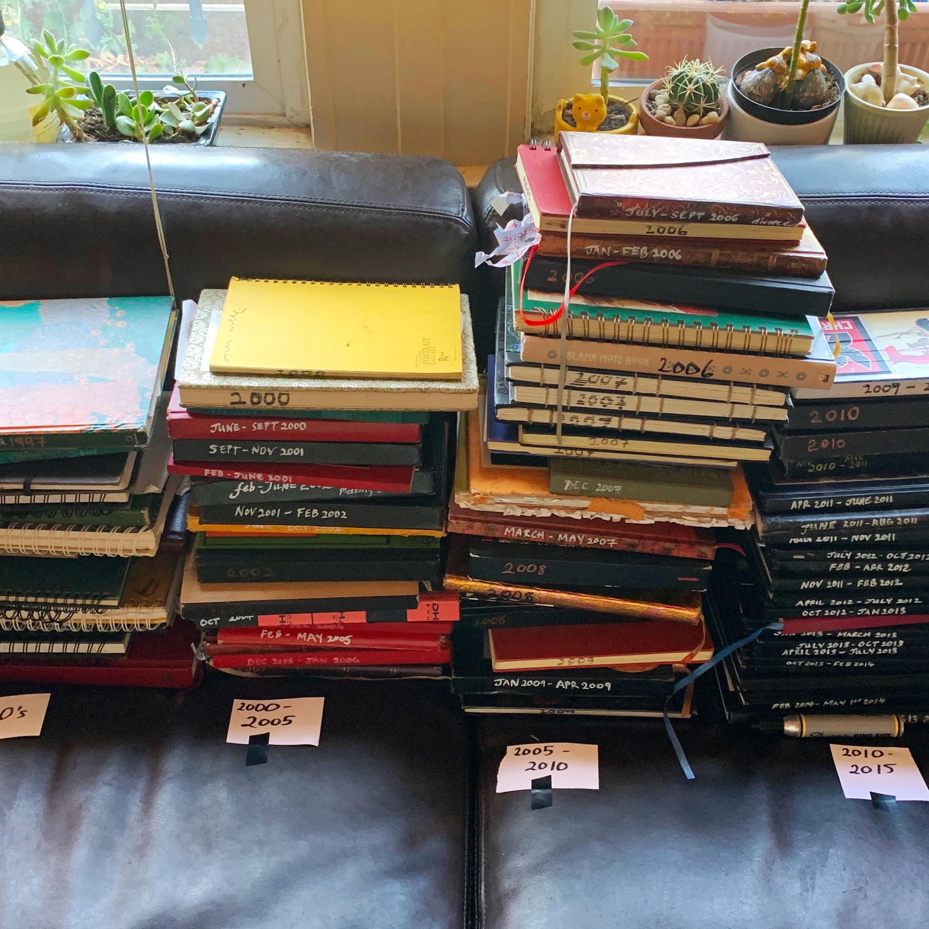 Multiple stacks of Nayomi Munaweera's journals separated by decades lying on her couch