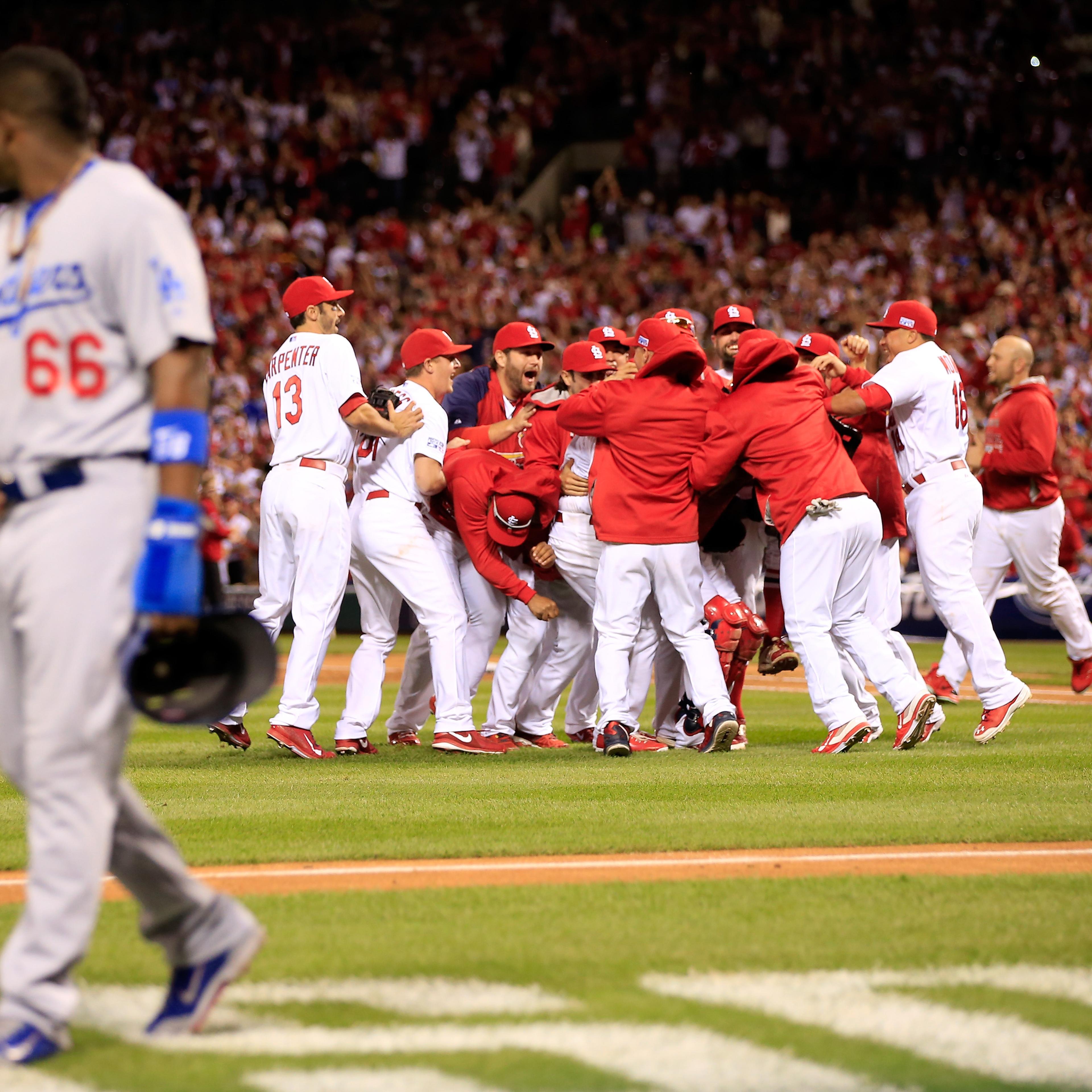 The St. Louis Cardinals celebrate after defeating the Los Angeles Dodgers as Yasiel Puig of the Los Angeles Dodgers walks off the field in Game Four of the National League Divison Series at Busch Stadium on Oct. 7, 2014 in St Louis.