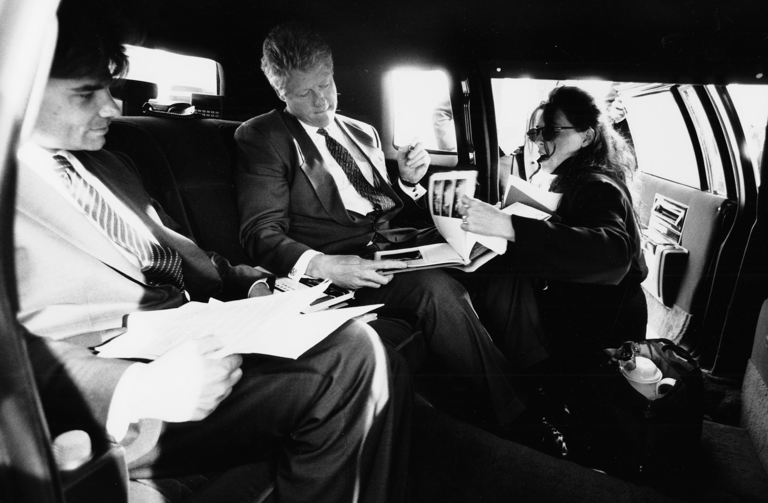 President Clinton in a limousine with George Stephanopoulos and Wendy Smith, signing autographs during a Presidential trip
