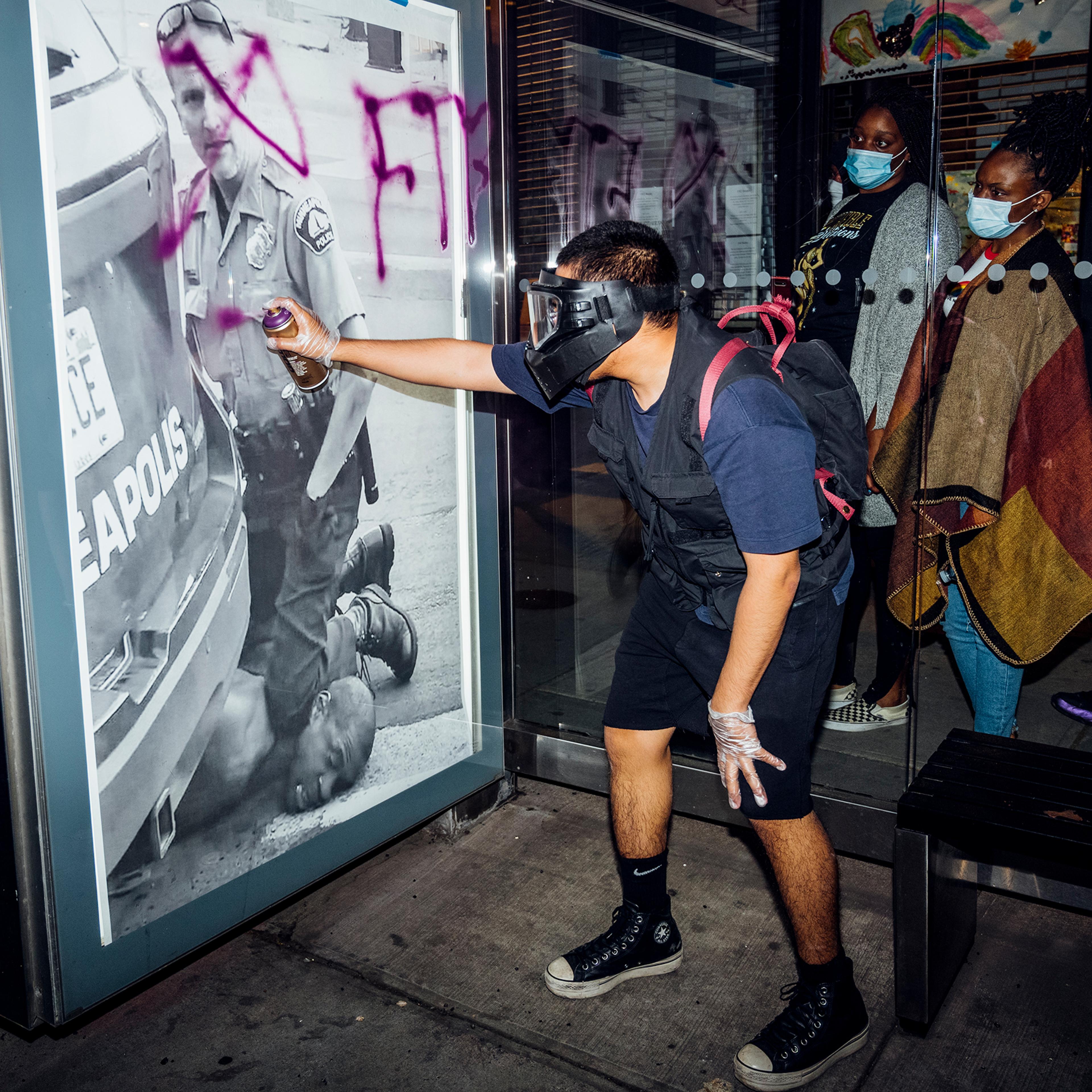 A demonstrator spray-paints a poster of Derek Chauvin’s knee on George Floyd’s neck on May 31. “Out of nowhere, this guy pulled out a purple spray can and just started writing on it. These ladies were walking by and paused to look at it. They were lookin