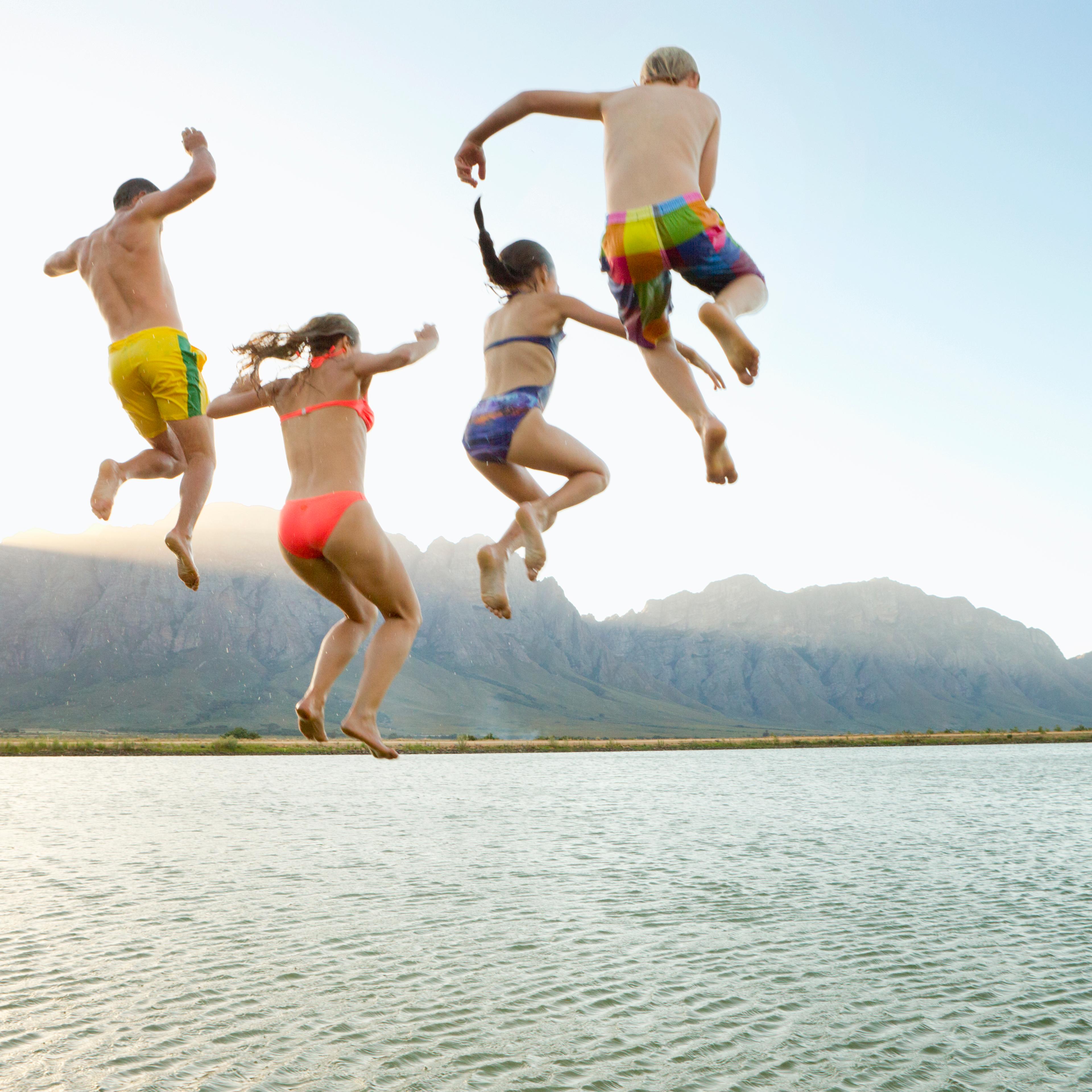 Family, in swimwear, jumping into a lake from a jetty