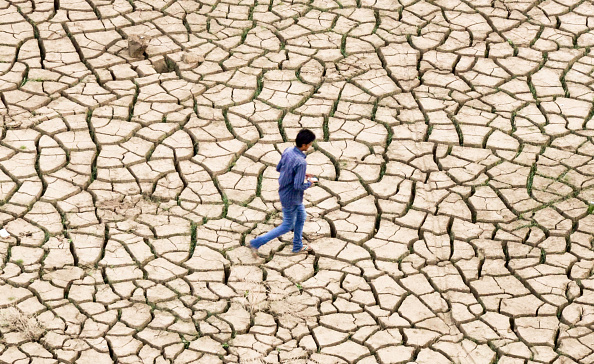 An Indian youth walks over dried mud on the banks of a river