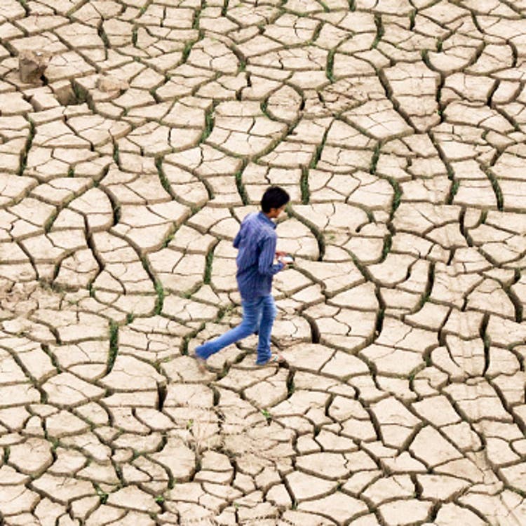 An Indian youth walks over dried mud on the banks of a river