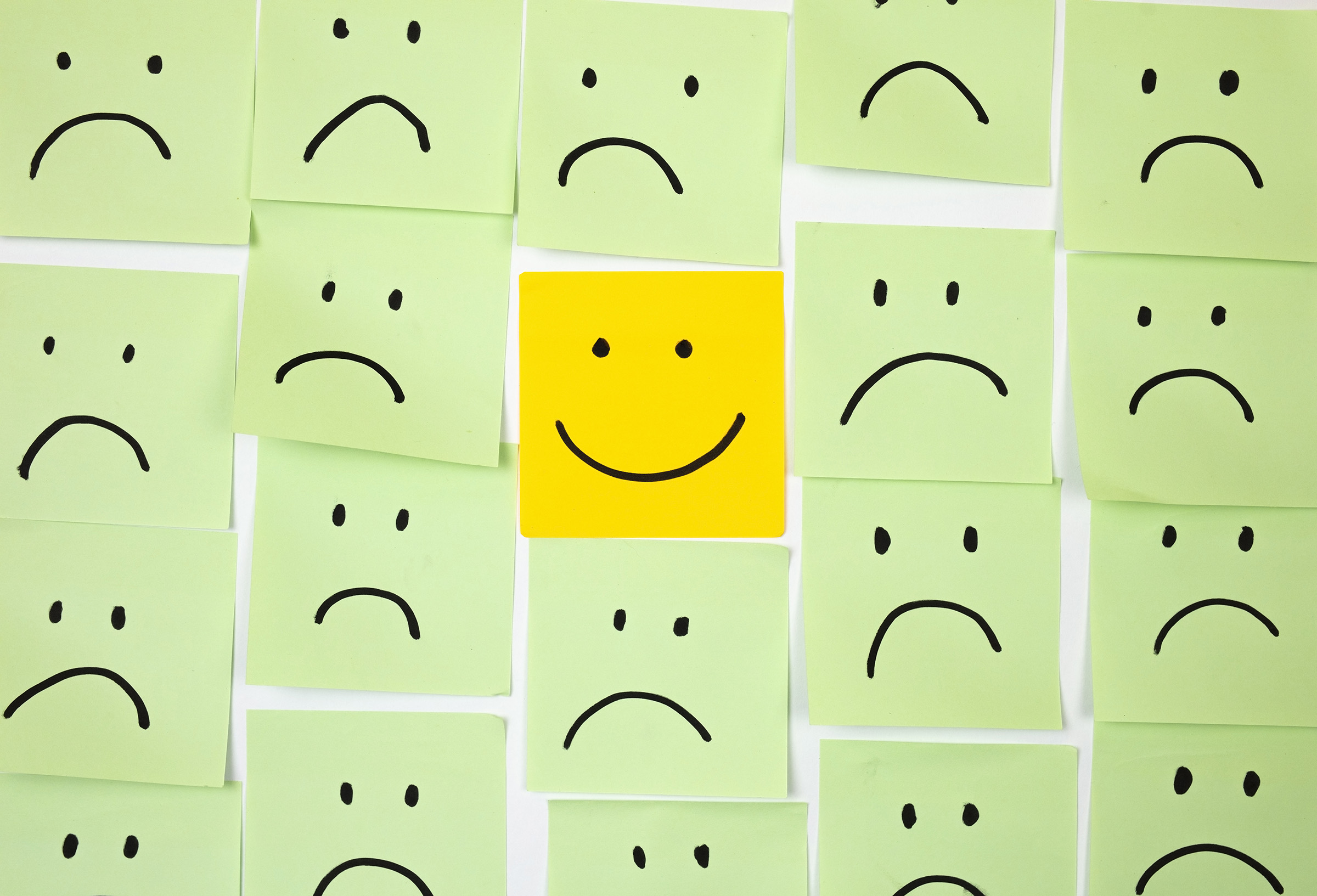 Sad faces on sticky notes with one happy one