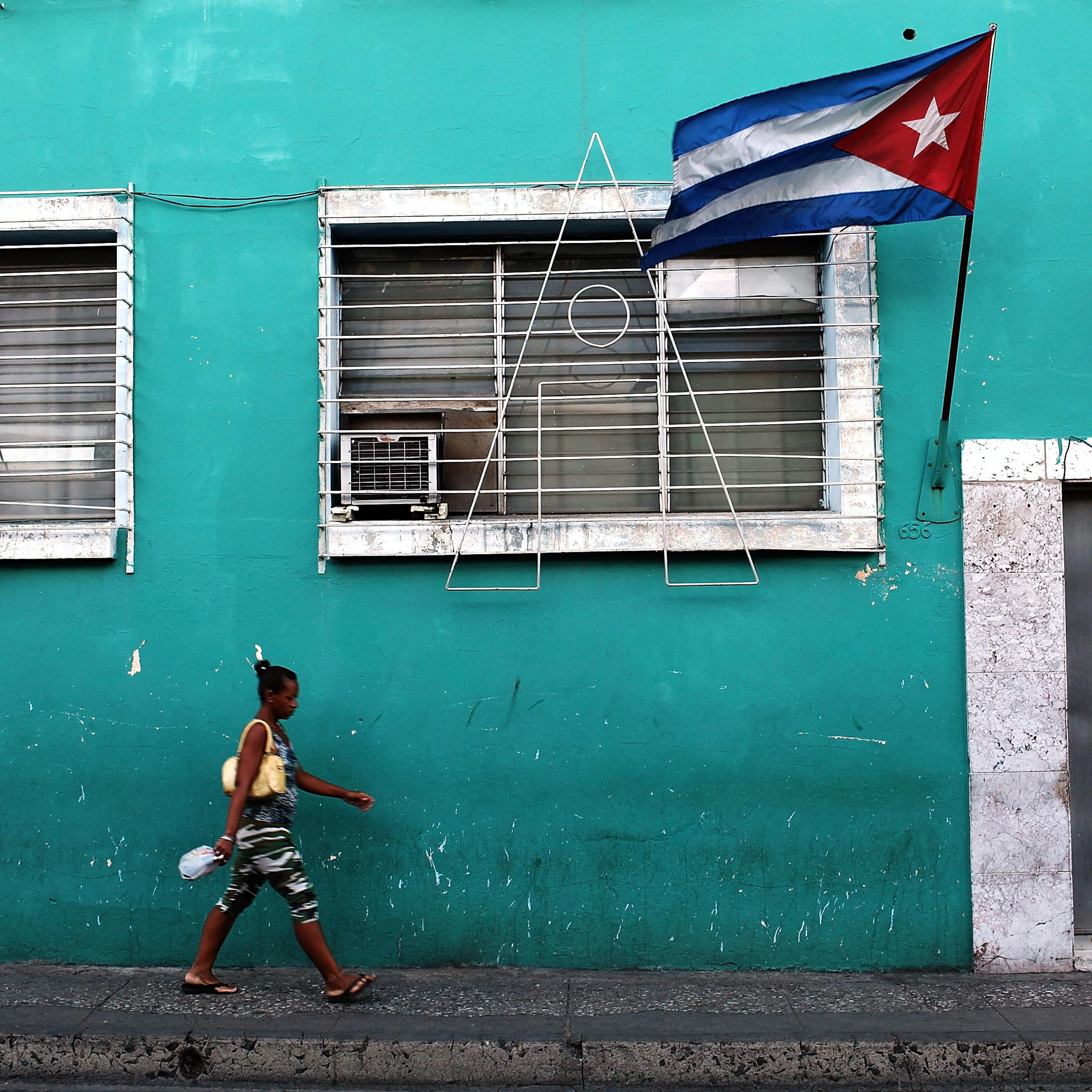 A woman walks under a Cuban flag on March 22, 2012 in Santiago de Cuba, Cuba.