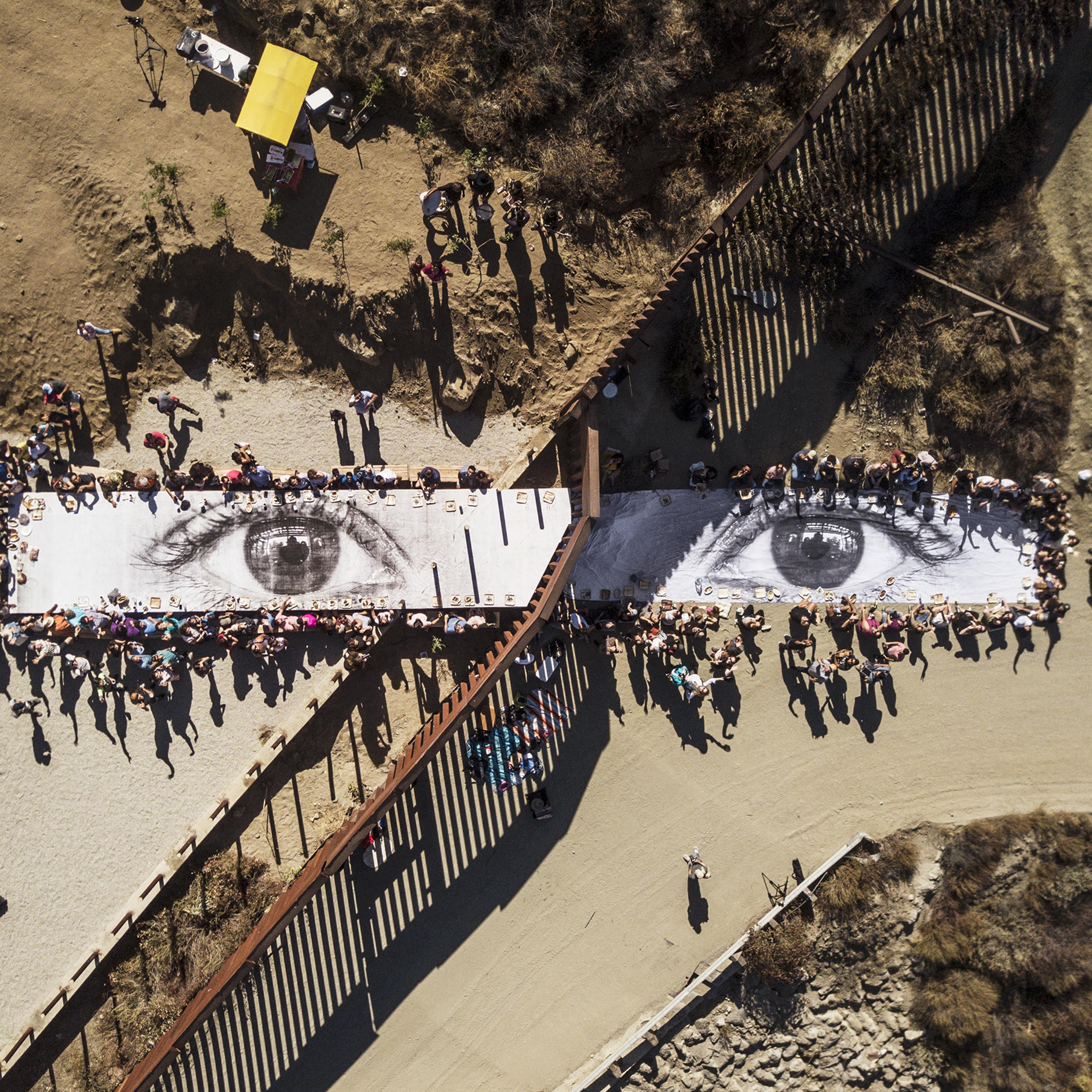A picnic takes place on JR’s Giant Picnic, a photograph of the eyes of a Dreamer at the U.S.-Mexico border in Tecate, Mexico, on Oct. 8