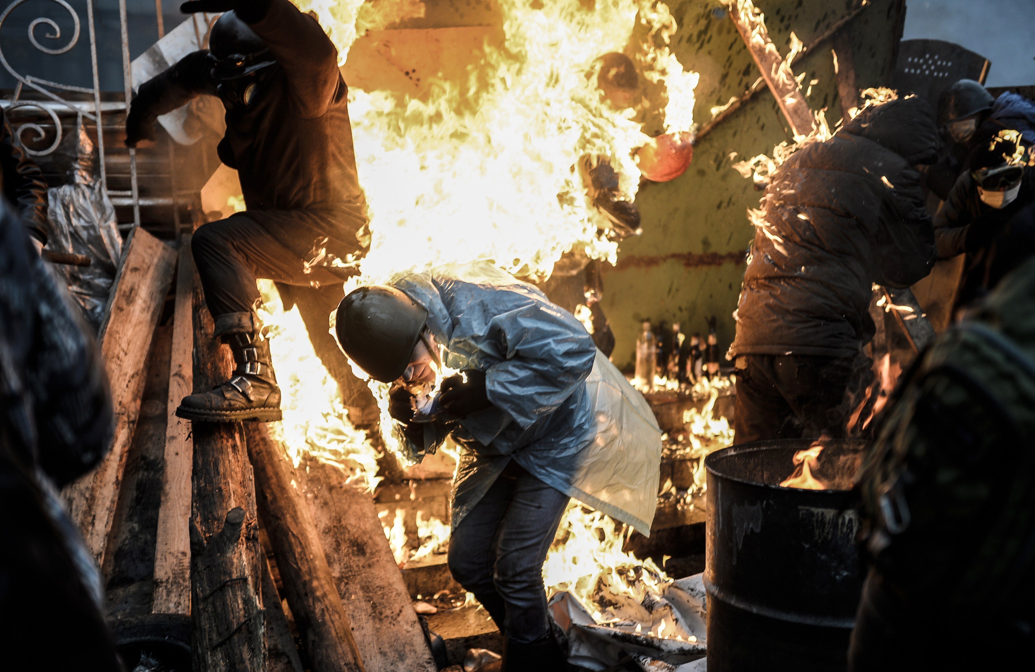 Protesters try to protect themselves from fire as they stand behind burning barricades during clashes with police on February 20, 2014 in Kiev.