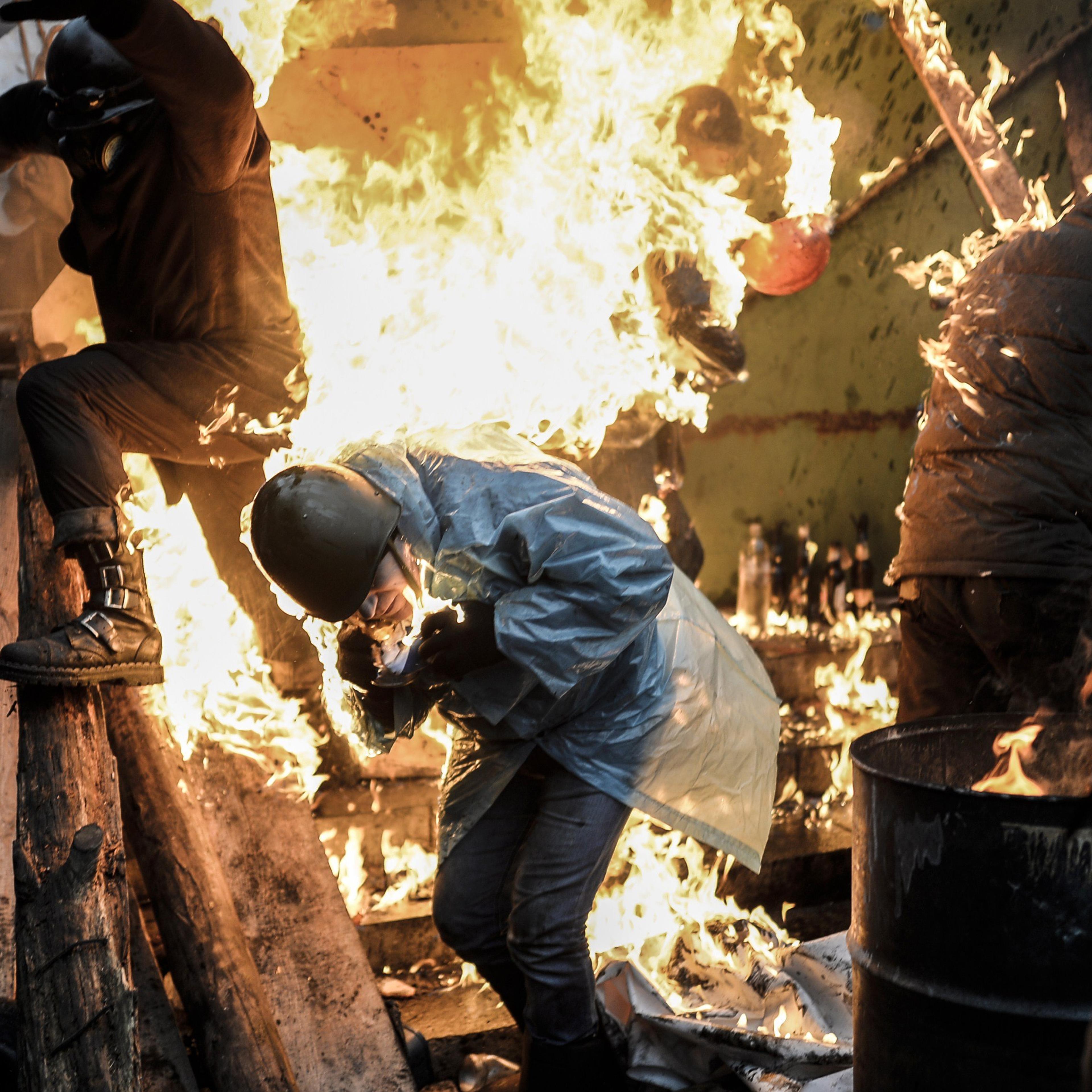 Protesters try to protect themselves from fire as they stand behind burning barricades during clashes with police on February 20, 2014 in Kiev.