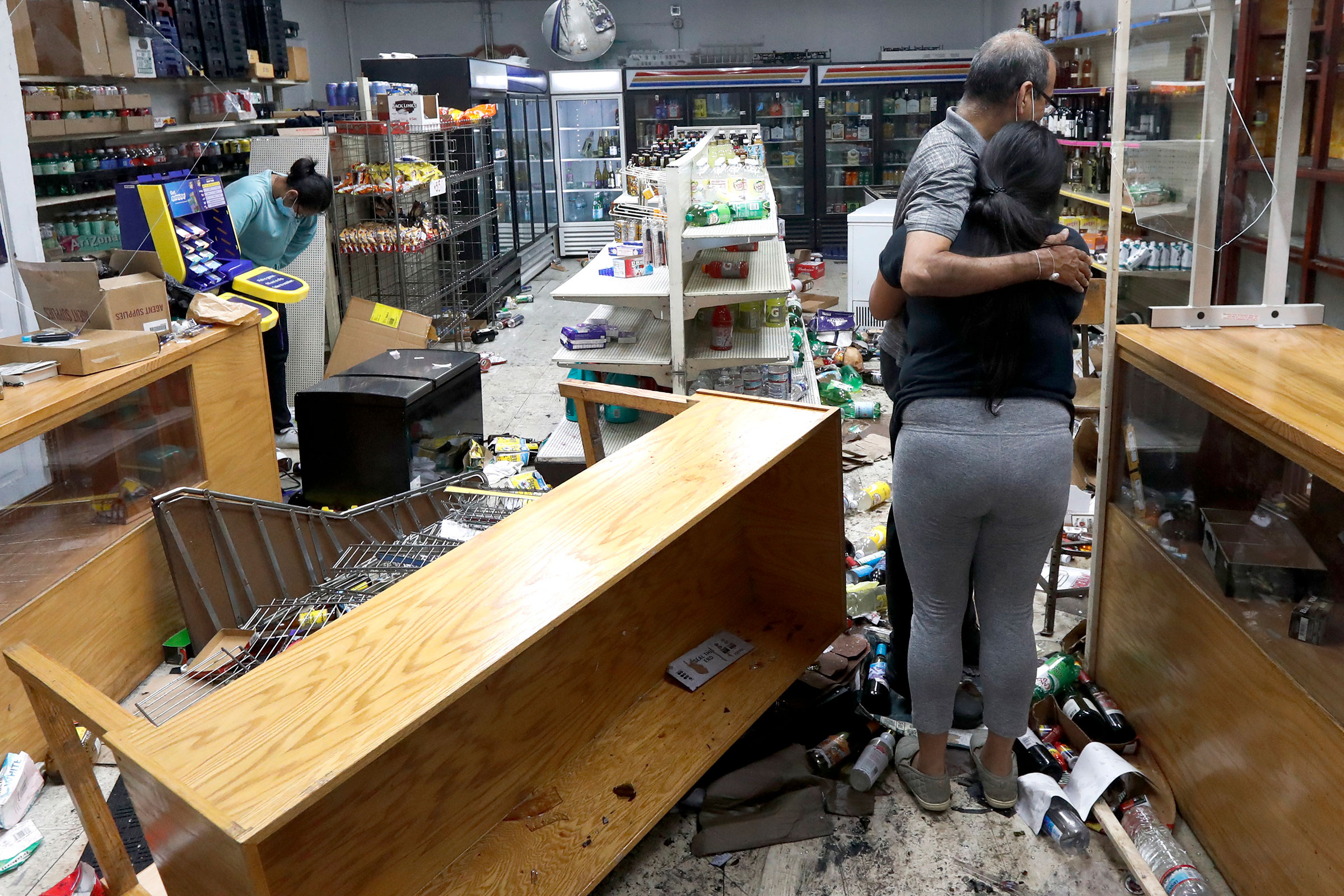 Yogi Dalal hugs his daughter Jigisha as his other daughter Kajal, left, bows her head at the family food and liquor store on, Aug. 10, 2020, after the family business was vandalized in Chicago