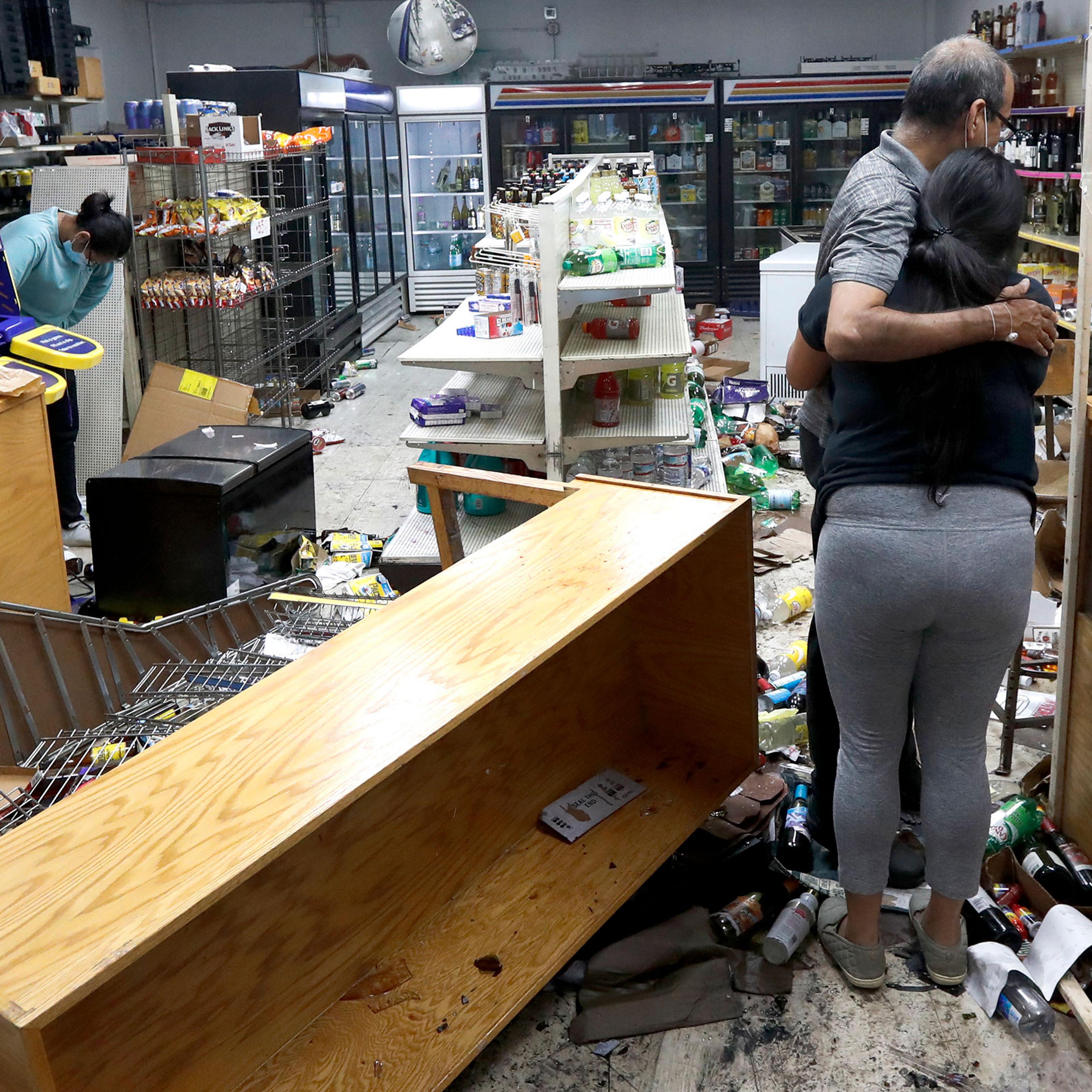 Yogi Dalal hugs his daughter Jigisha as his other daughter Kajal, left, bows her head at the family food and liquor store on, Aug. 10, 2020, after the family business was vandalized in Chicago