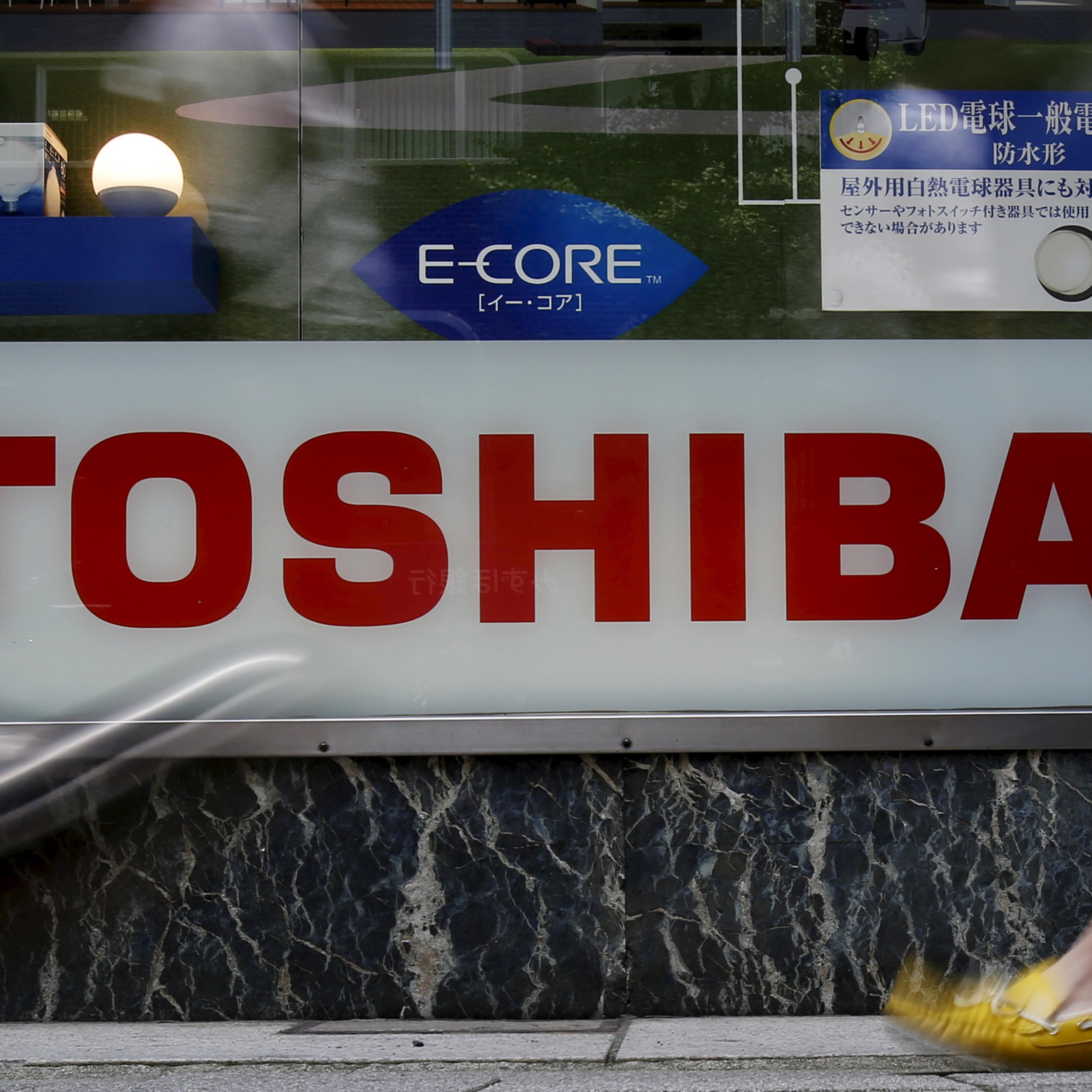 Pedestrians walk past a logo of Toshiba Corp outside an electronics retailer in Tokyo