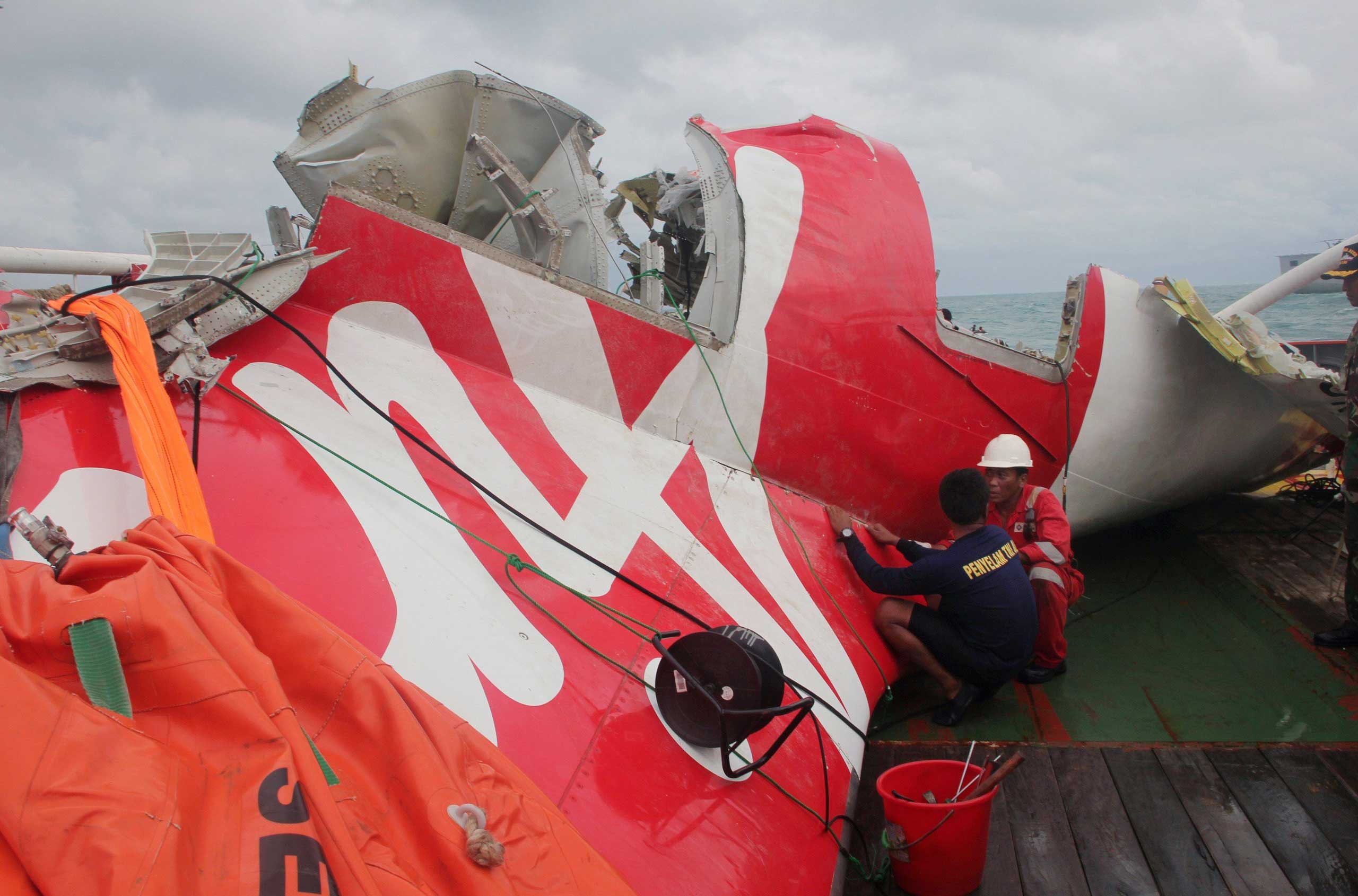 An Indonesian diver and an official examine the wreckage from AirAsia flight QZ8501 after it was lifted into the Crest Onyx ship at sea, near Indonesia on Jan. 10, 2015.