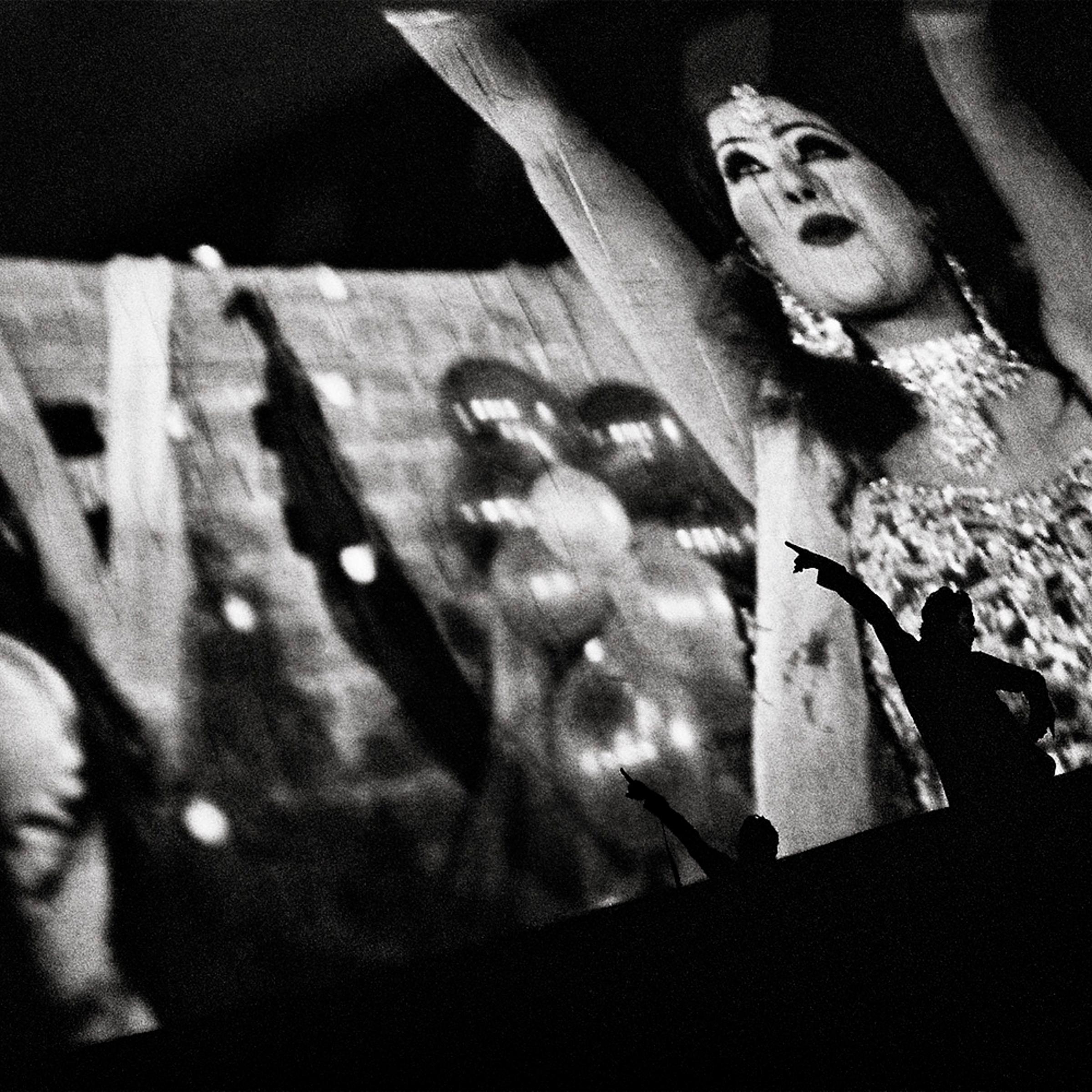 A Pashtun man dances on stage along to the musical number behind him on the screen. He is cheered on by the crowd.
