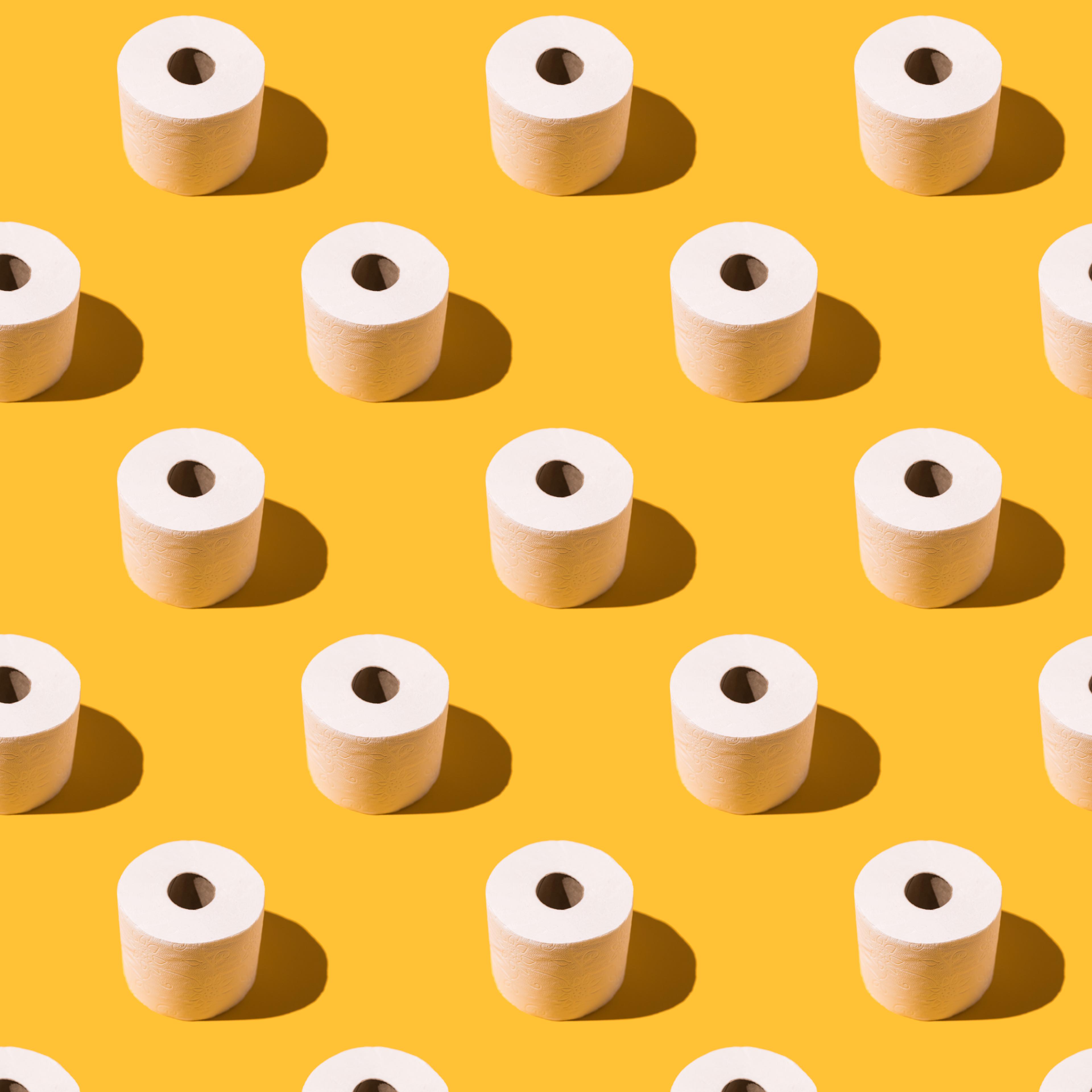 Pattern of white toilet paper rolls on yellow background. Concept of going to the bathroom, cleaning and pooping and peeing.