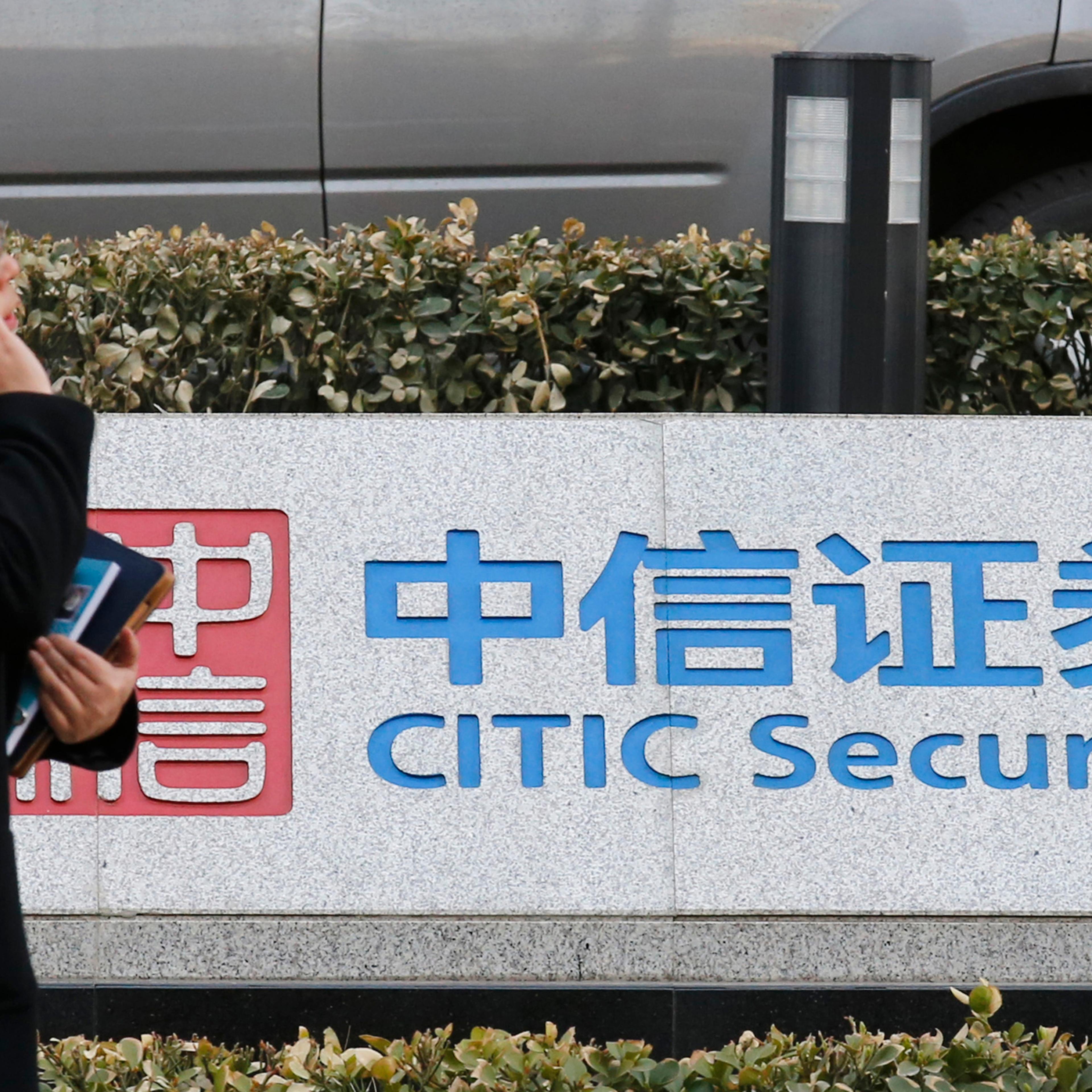 A woman walks past a signboard of CITIC Securities at its head office in Beijing