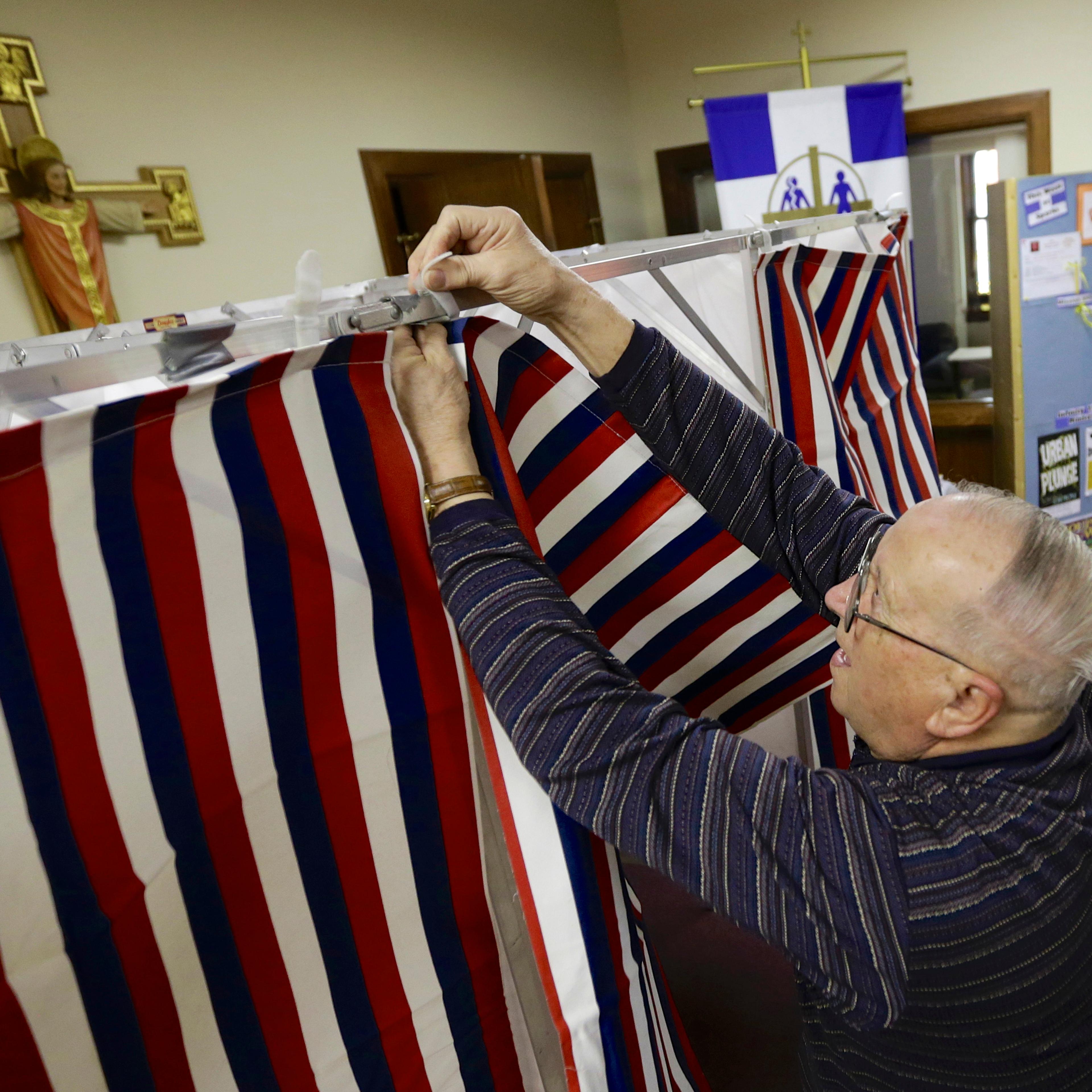 Election official Robert Buresh attaches the curtain to a polling booth at the Salem Lutheran Church polling station in Fremont, Neb., on Feb. 11, 2014.