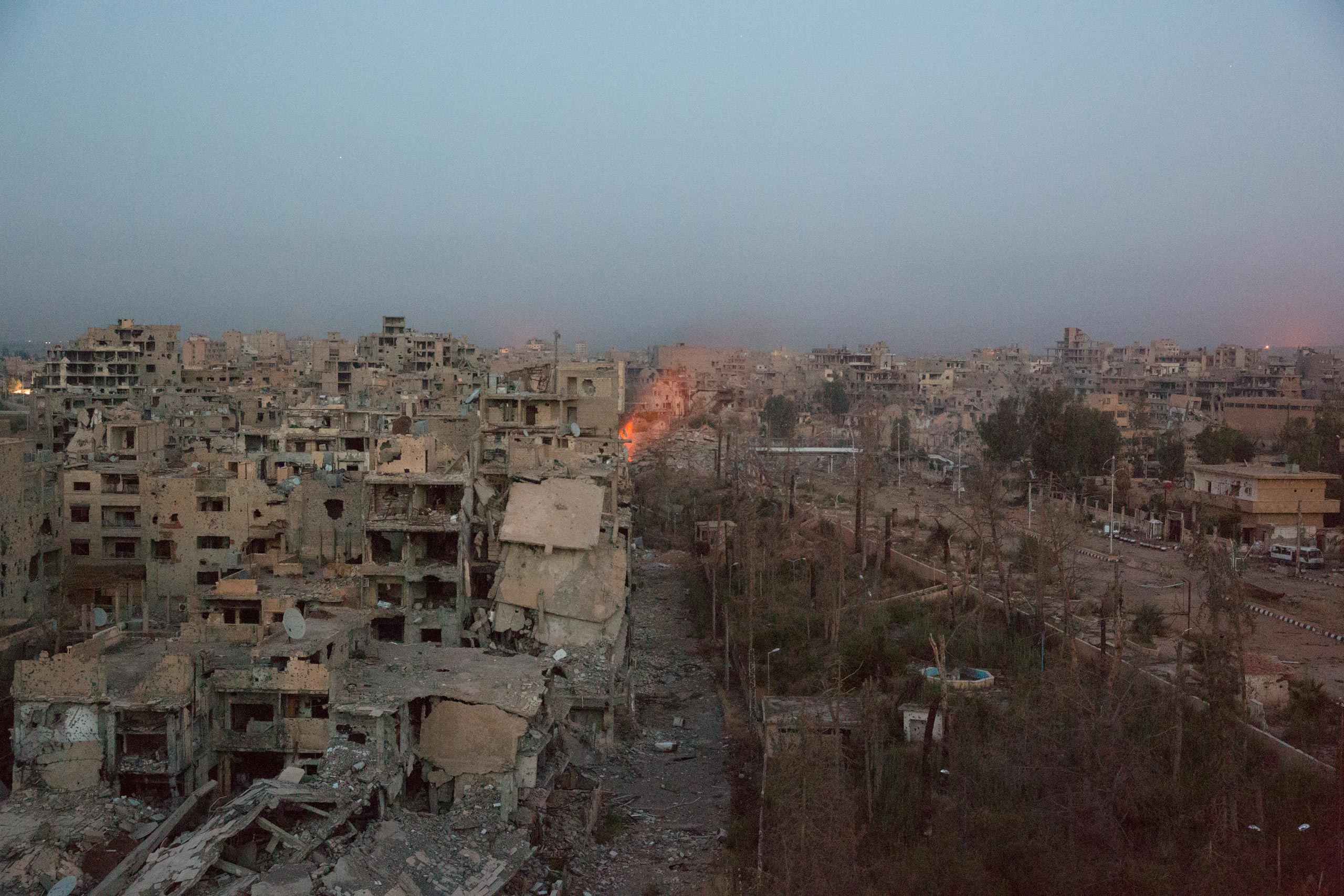 The ISIS-controlled area of Deir-ez Zor appears to be greatly damaged by artillery and aerial bombing, while the government section of the city has suffered relatively minor damage.  An explosion was possibly caused by a rocket-propelled grenade fired from a government position, May 24, 2015.
