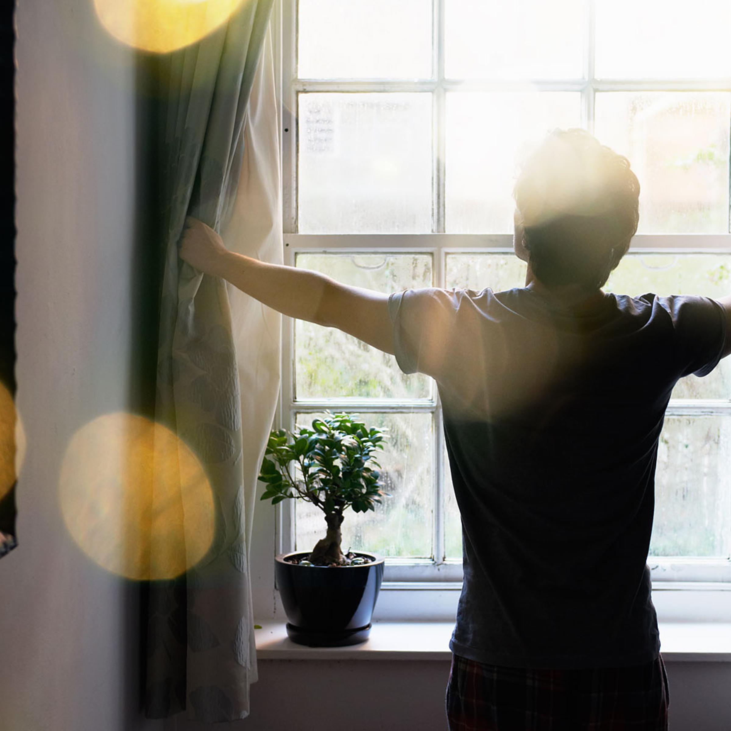 man opening curtains in the morning