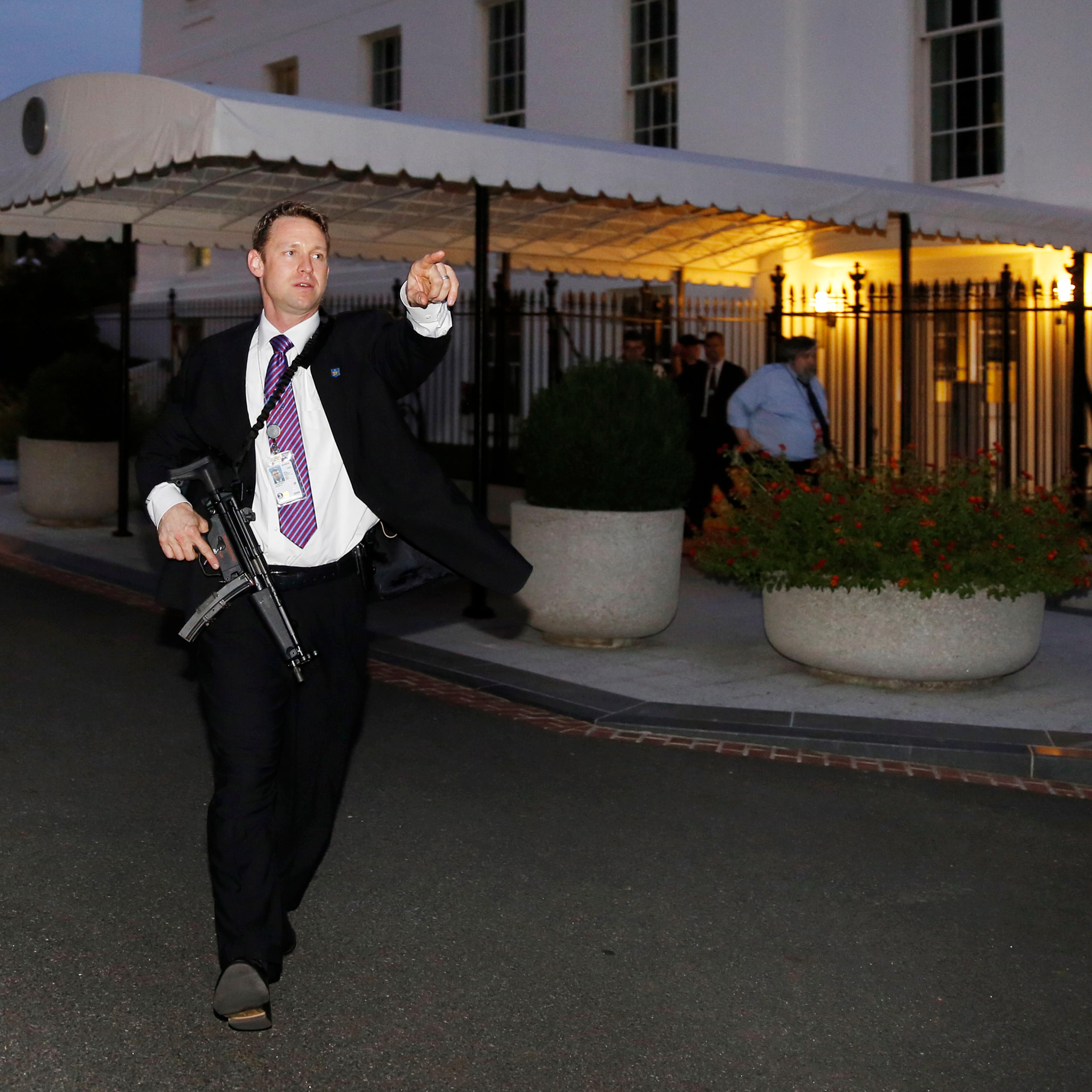 A U.S. Secret Service agent with an automatic rifle hurries people to evacuate the White House complex over a security alert moments after President Barack Obama and his family left for the presidential retreat, Camp David, in Maryland