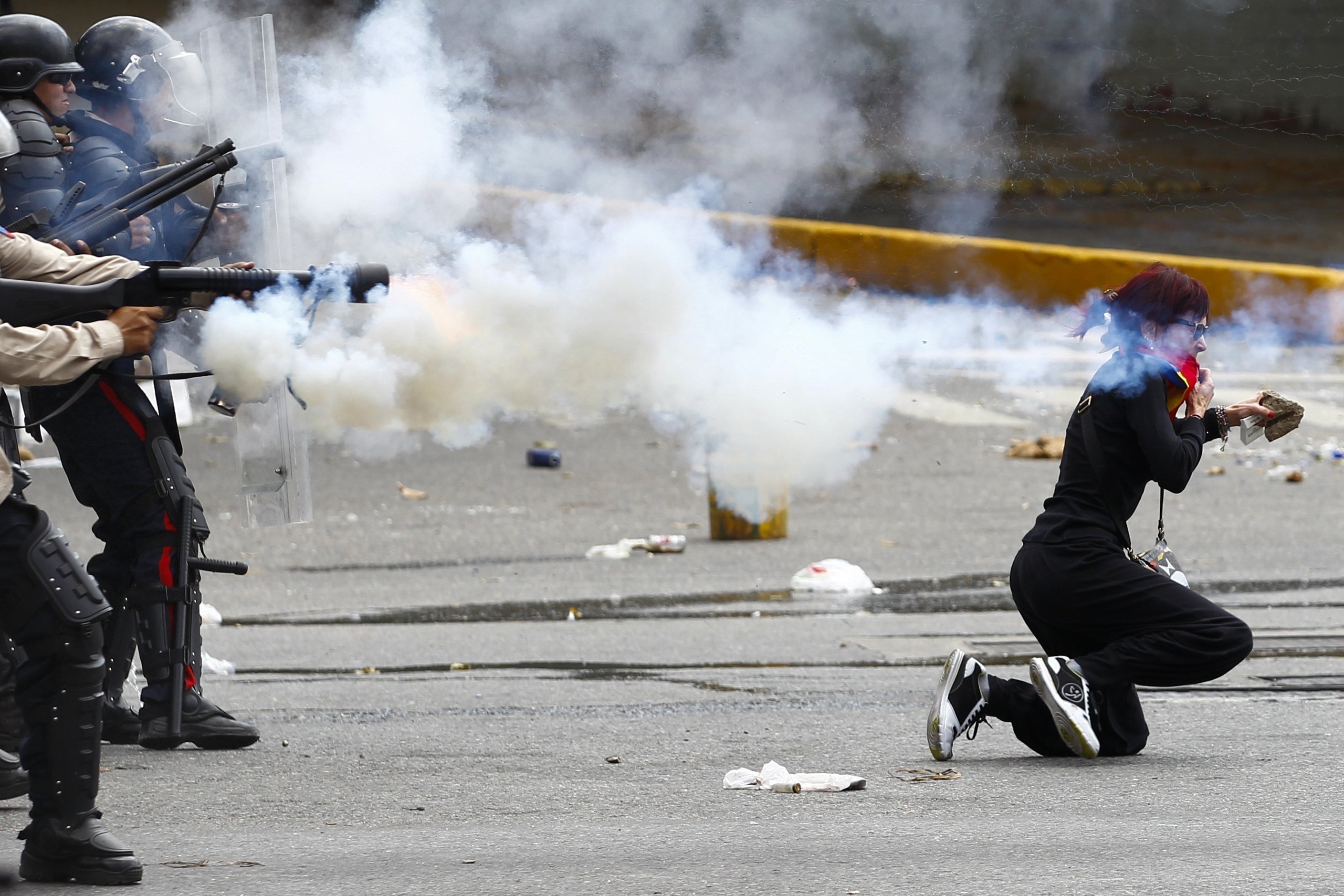 An antigovernment protester ducks for cover as Venezuelan police fire tear gas during riots in Caracas
