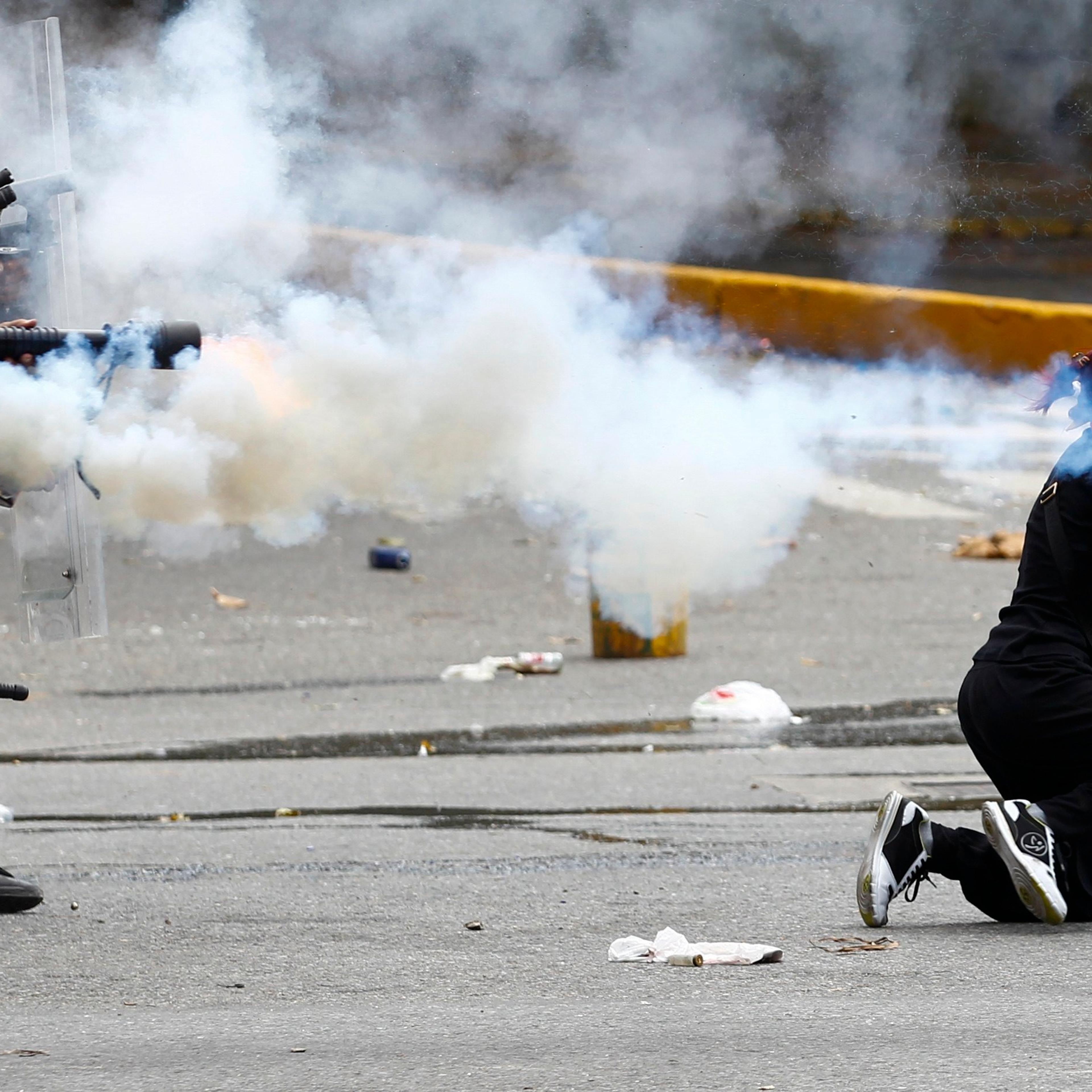 An antigovernment protester ducks for cover as Venezuelan police fire tear gas during riots in Caracas