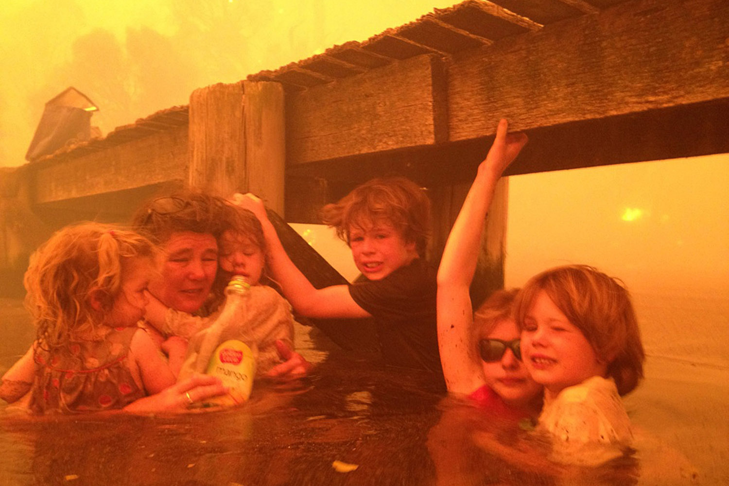 Jan. 4, 2013. Tammy Holmes, second from left, and her grandchildren, two-year-old Charlotte Walker, left, four-year-old Esther Walker, third from left, nine-year-old Liam Walker, eleven-year-old Matilda, second from right, and six-year-old Caleb Walker, right, take refuge under a jetty as a wildfire rages near-by in the Tasmanian town of Dunalley, Australia.