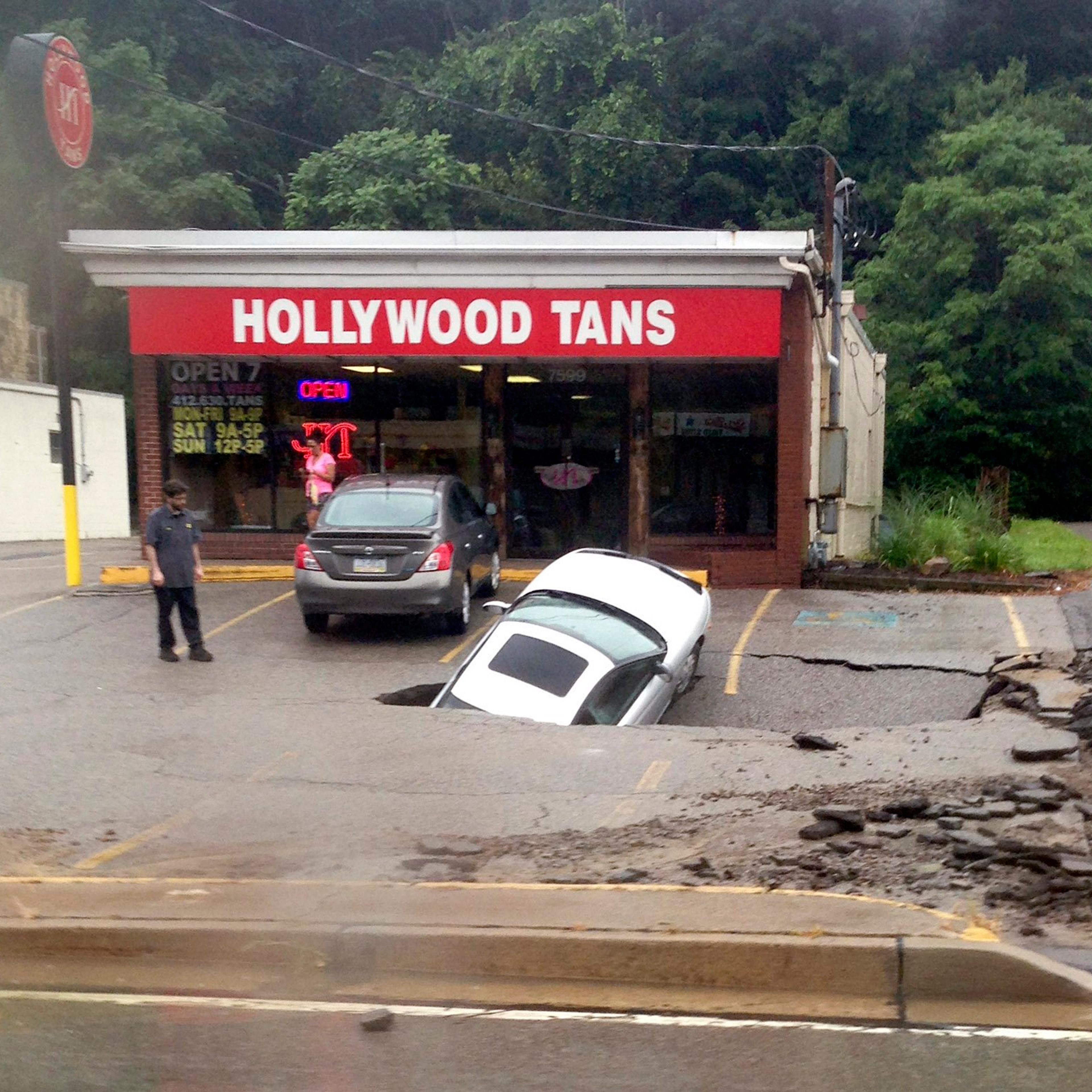 A man looks at a car as it falls into a sinkhole on McKnight Road in Ross Township of Pittsburgh on Aug. 12, 2014.