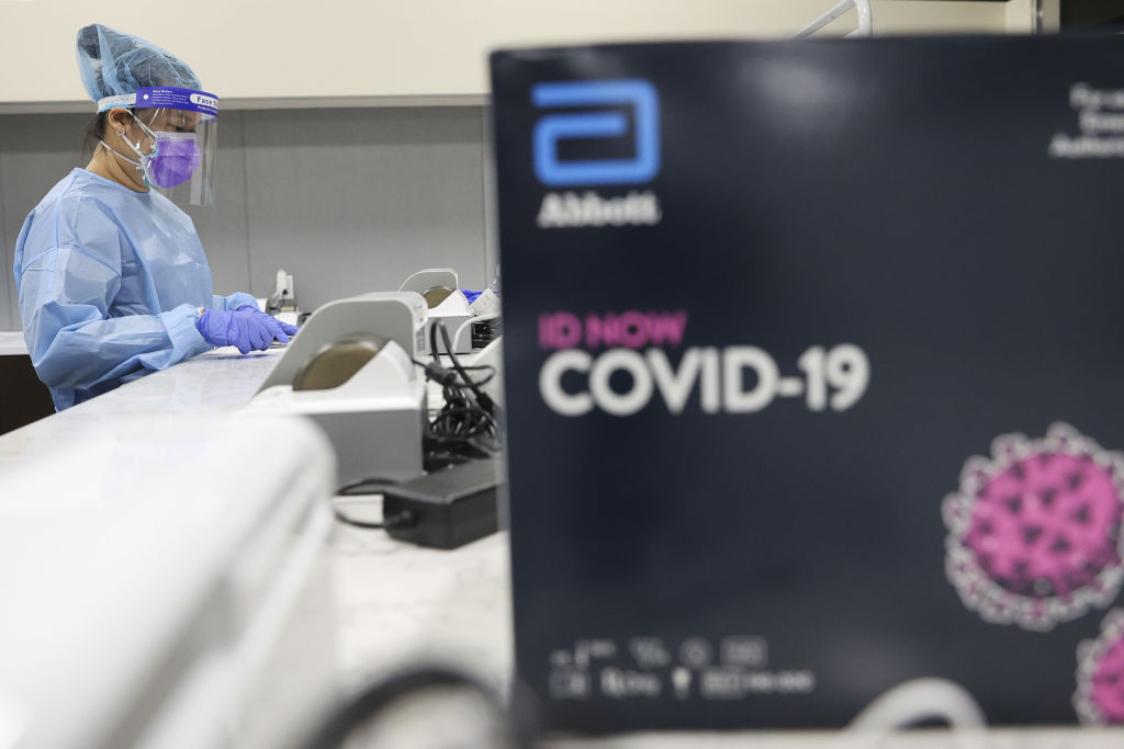 A healthcare worker wearing personal protective equipment (PPE) uses a Abbott Laboratories ID NOW rapid test machine during a United Airlines COVID-19 test pilot program at Newark Liberty International Airport in Newark,