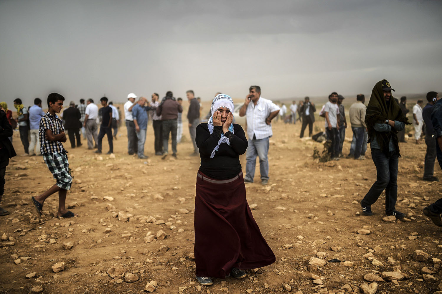 A Syrian Kurdish woman wipes her eyes during a dust storm on a hill where she and others stand watching clashes between jihadists of the Islamic State and Kurdish fighters, at Swedi village some 6 miles west of Suruc in Sanliurfa province, on Sept. 24, 2