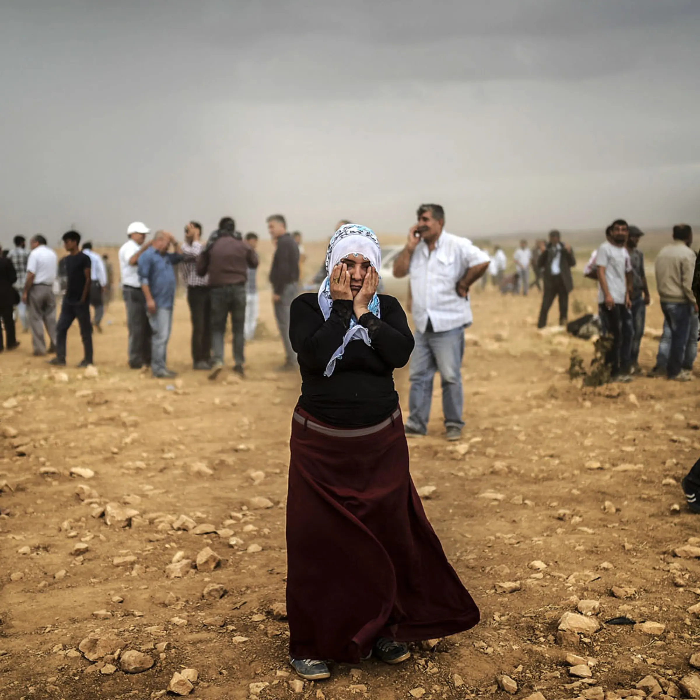 A Syrian Kurdish woman wipes her eyes during a dust storm on a hill where she and others stand watching clashes between jihadists of the Islamic State and Kurdish fighters, at Swedi village some 6 miles west of Suruc in Sanliurfa province, on Sept. 24, 2