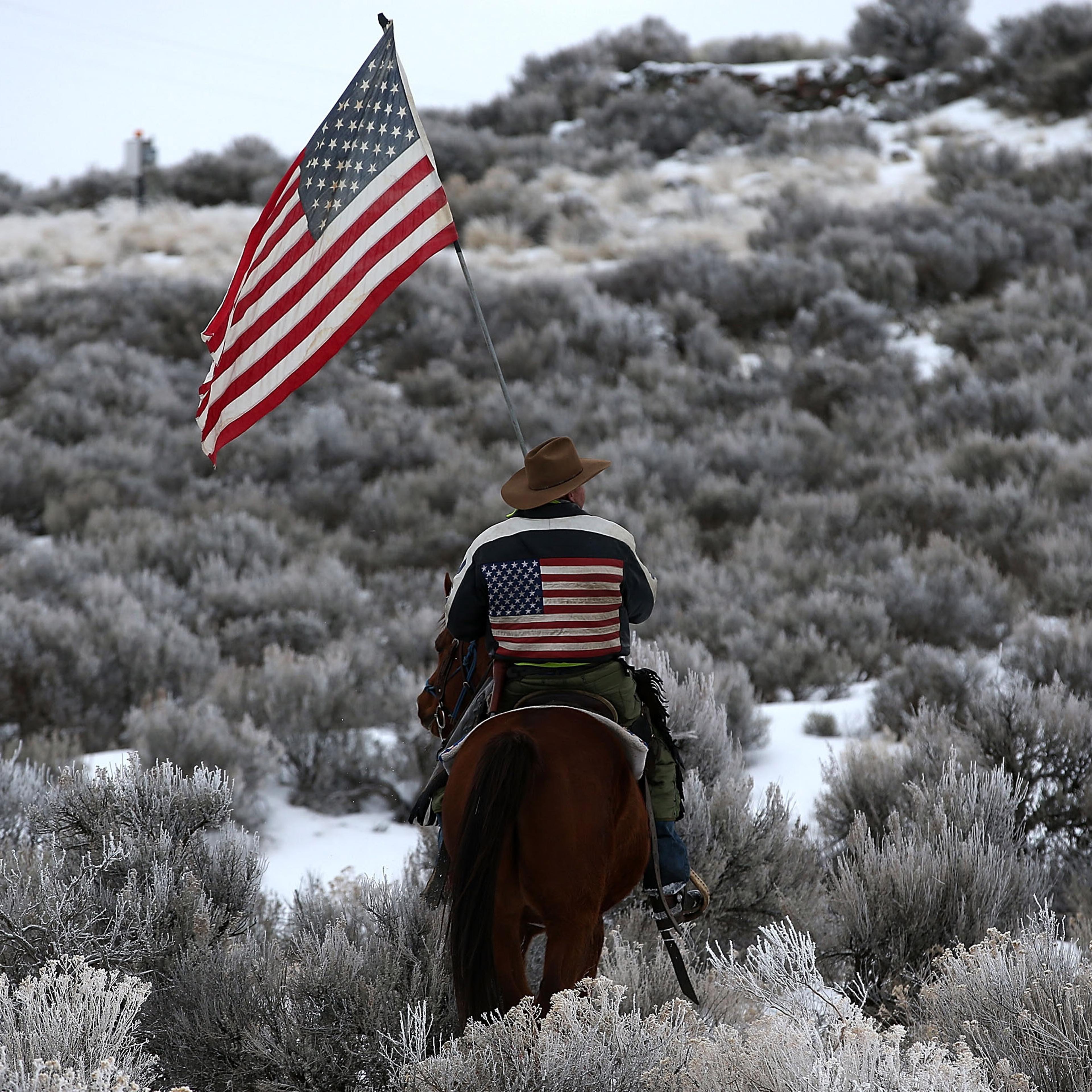 Dwayne Ehmer carries an American flag as he rides his horse on the Malheur National Wildlife Refuge near Burns, Ore., on Jan. 7, 2016.