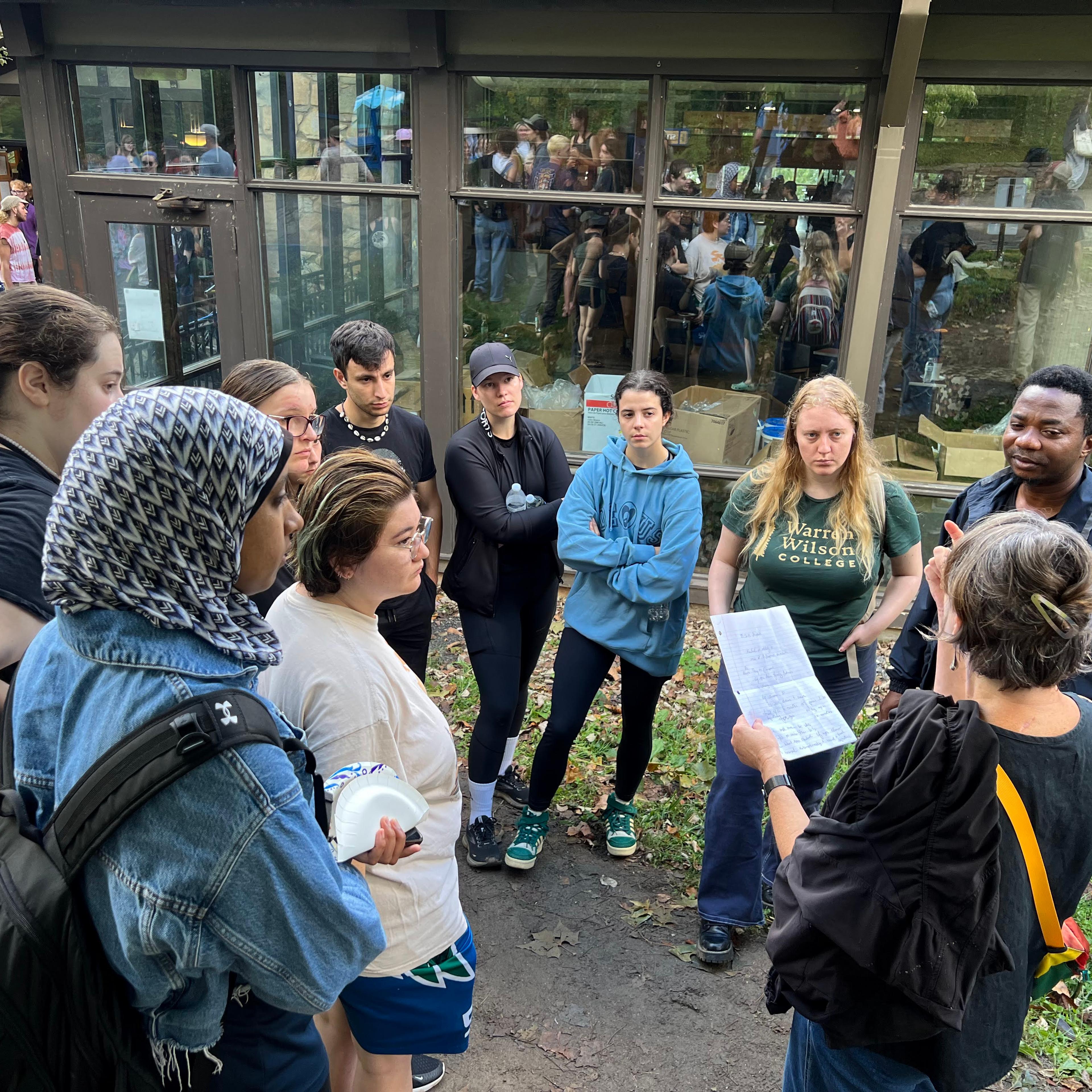 Several college students stand outside in a meeting.