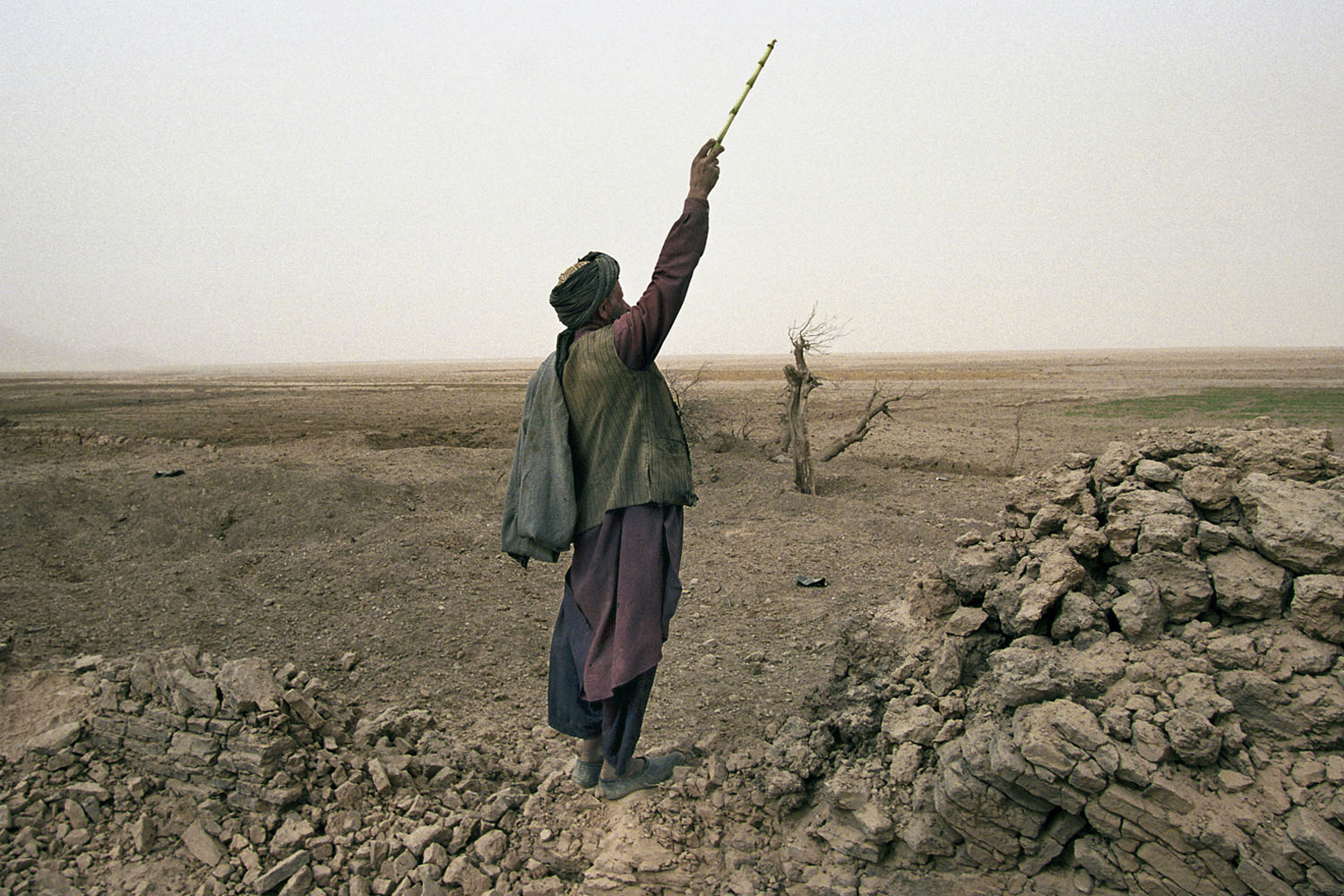 A local Afghan shepherd in Chowkar Karez shouts to his children to lead their flock of goats over to him. He stands on a destroyed wall of a village 80 kms north of Kandahar bombed flat two weeks before by US jets. November, 2001
