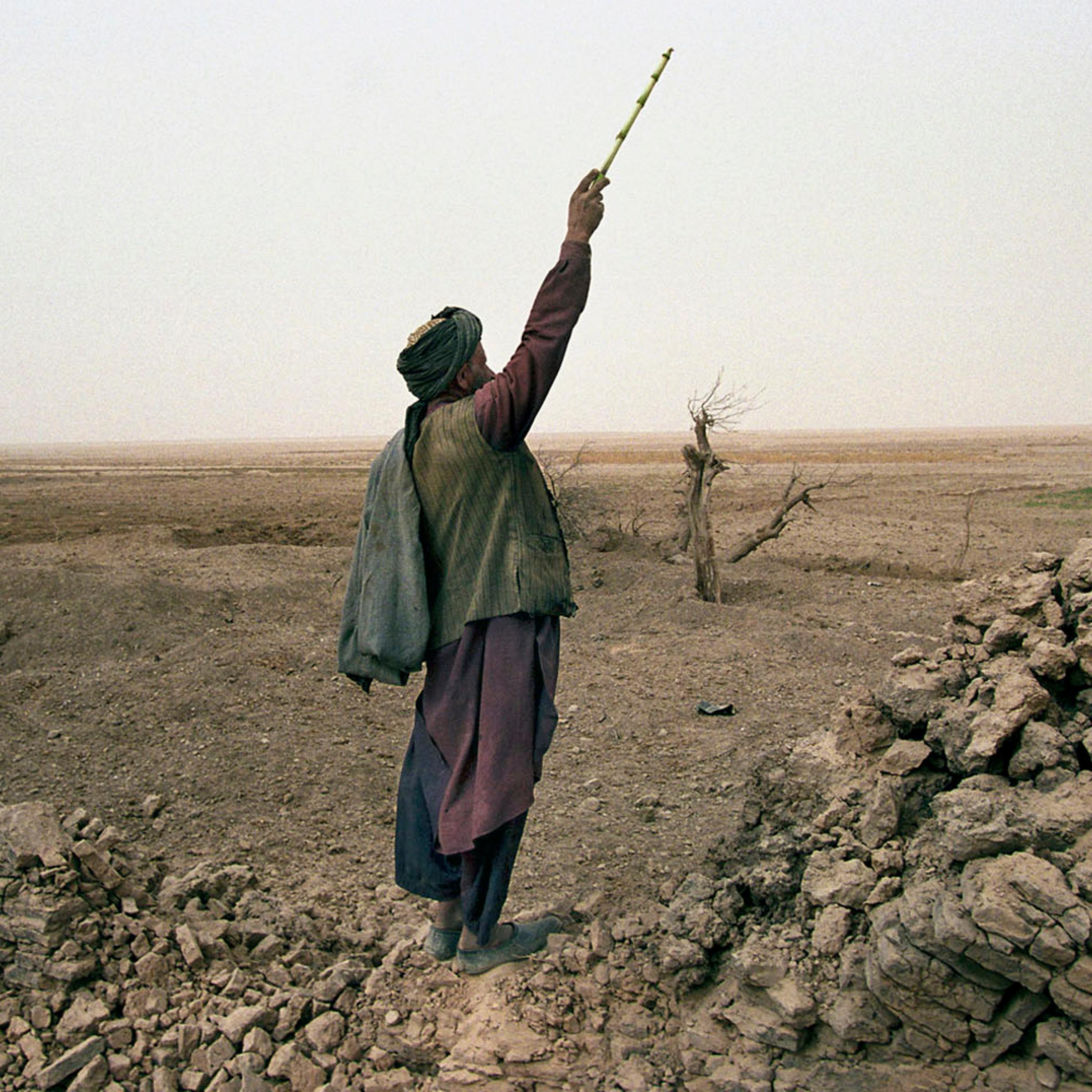 A local Afghan shepherd in Chowkar Karez shouts to his children to lead their flock of goats over to him. He stands on a destroyed wall of a village 80 kms north of Kandahar bombed flat two weeks before by US jets. November, 2001