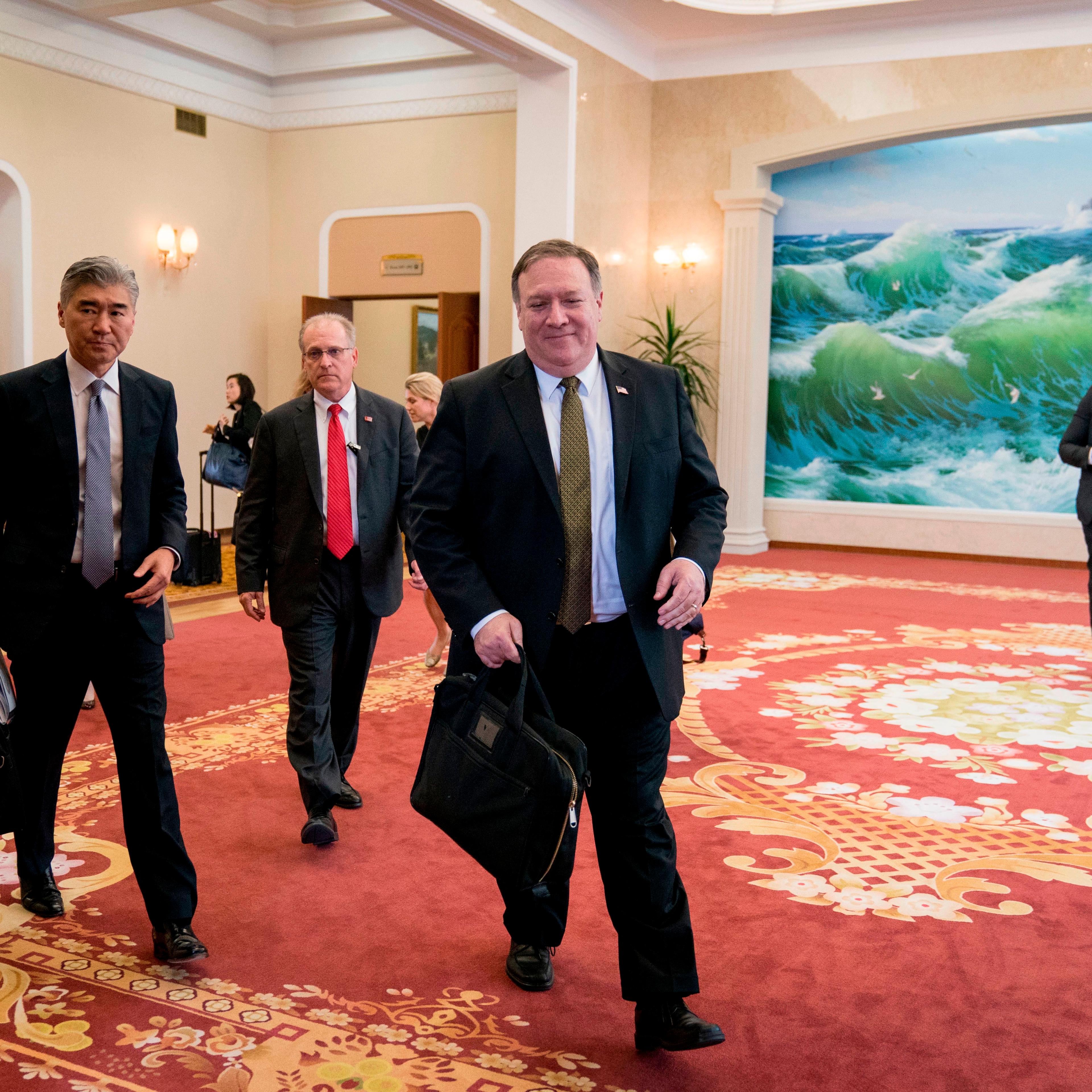 Michael Pompeo in a Guest House with three other men behind him. The carpet is red and there's a painting on the opposite wall