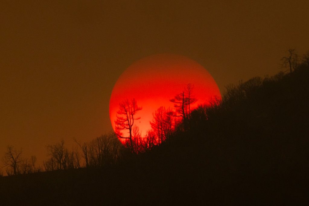 The sun sinks behind a smoky sky and burned forest at the Oak Fire on near Mariposa, California, on July 24, 2022. 