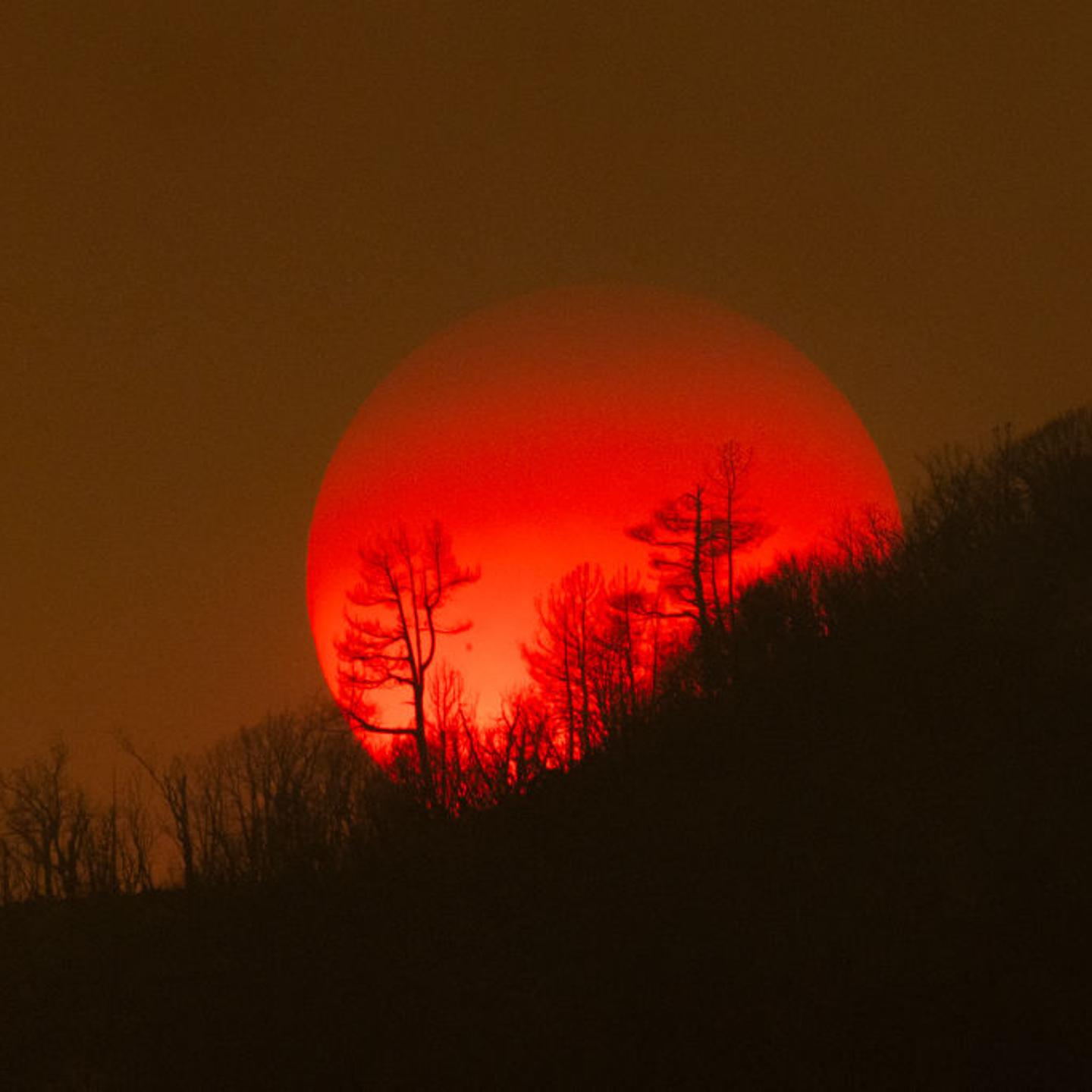 The sun sinks behind a smoky sky and burned forest at the Oak Fire on near Mariposa, California, on July 24, 2022.