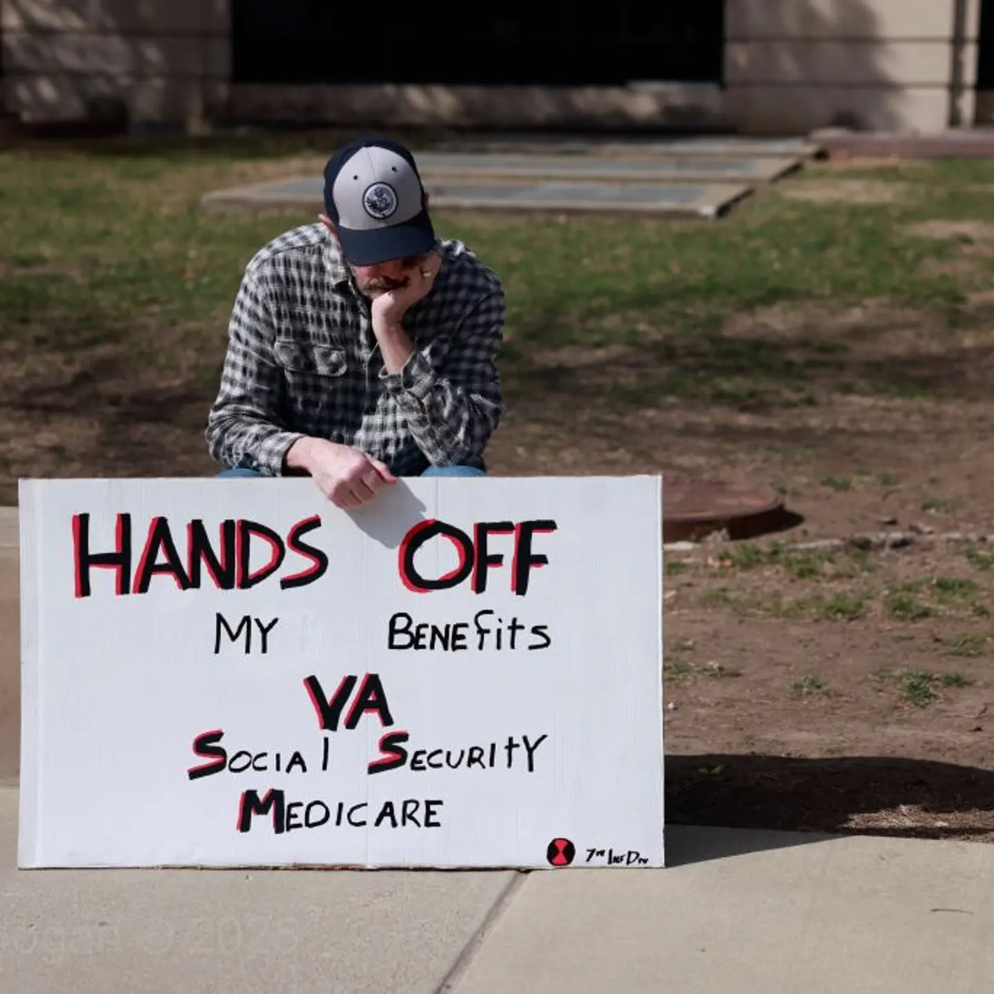 A protester sits with a sign reading, "Hands off my