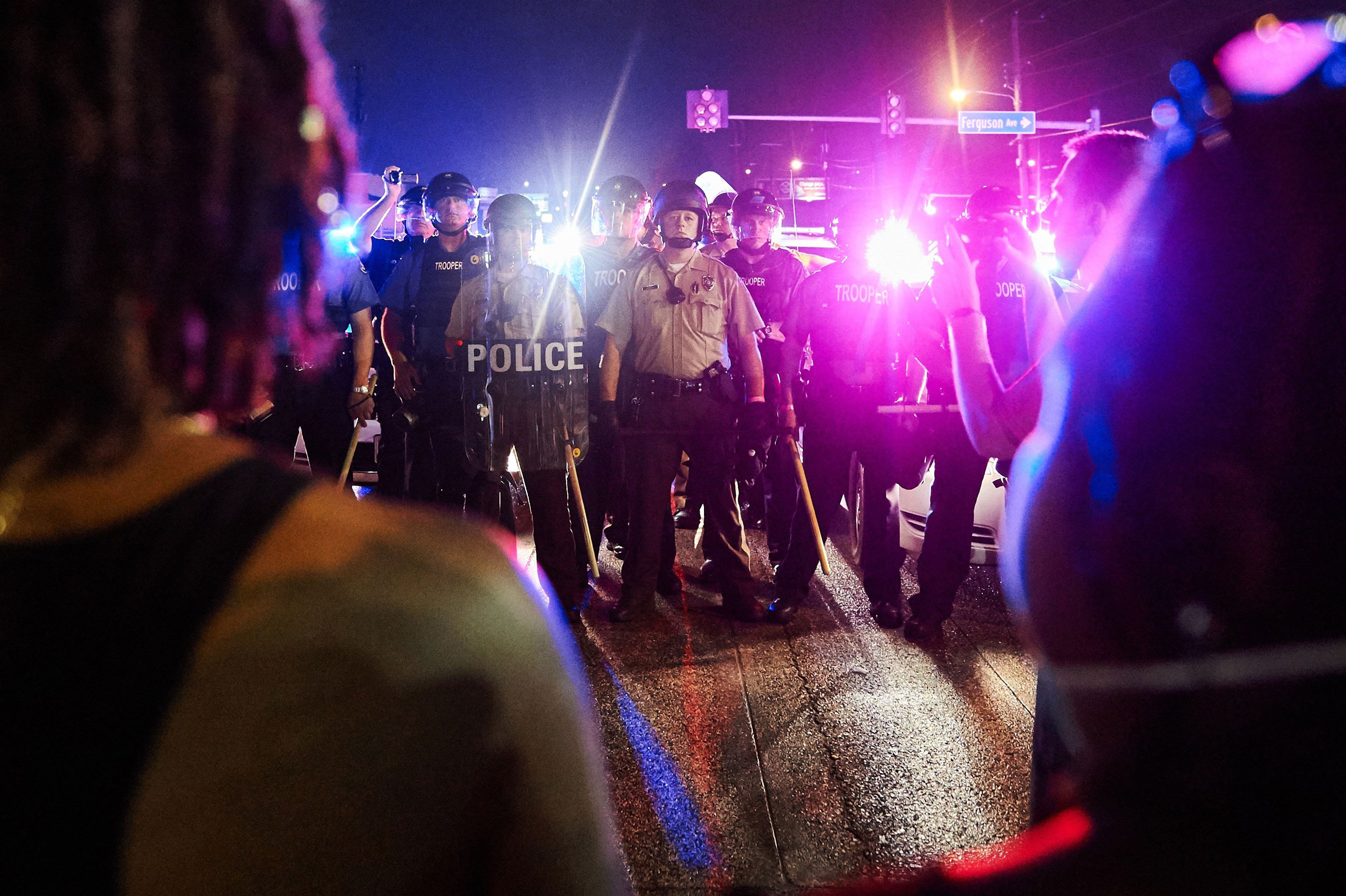 St. Louis County Police and Missouri State Highway Patrol troopers (C) stand guard as protesters (foreground) march on West Florissant Avenue in Ferguson, Missouri on August 9, 2015. A day of peaceful remembrance marking the anniversary of 18-year-old bl
