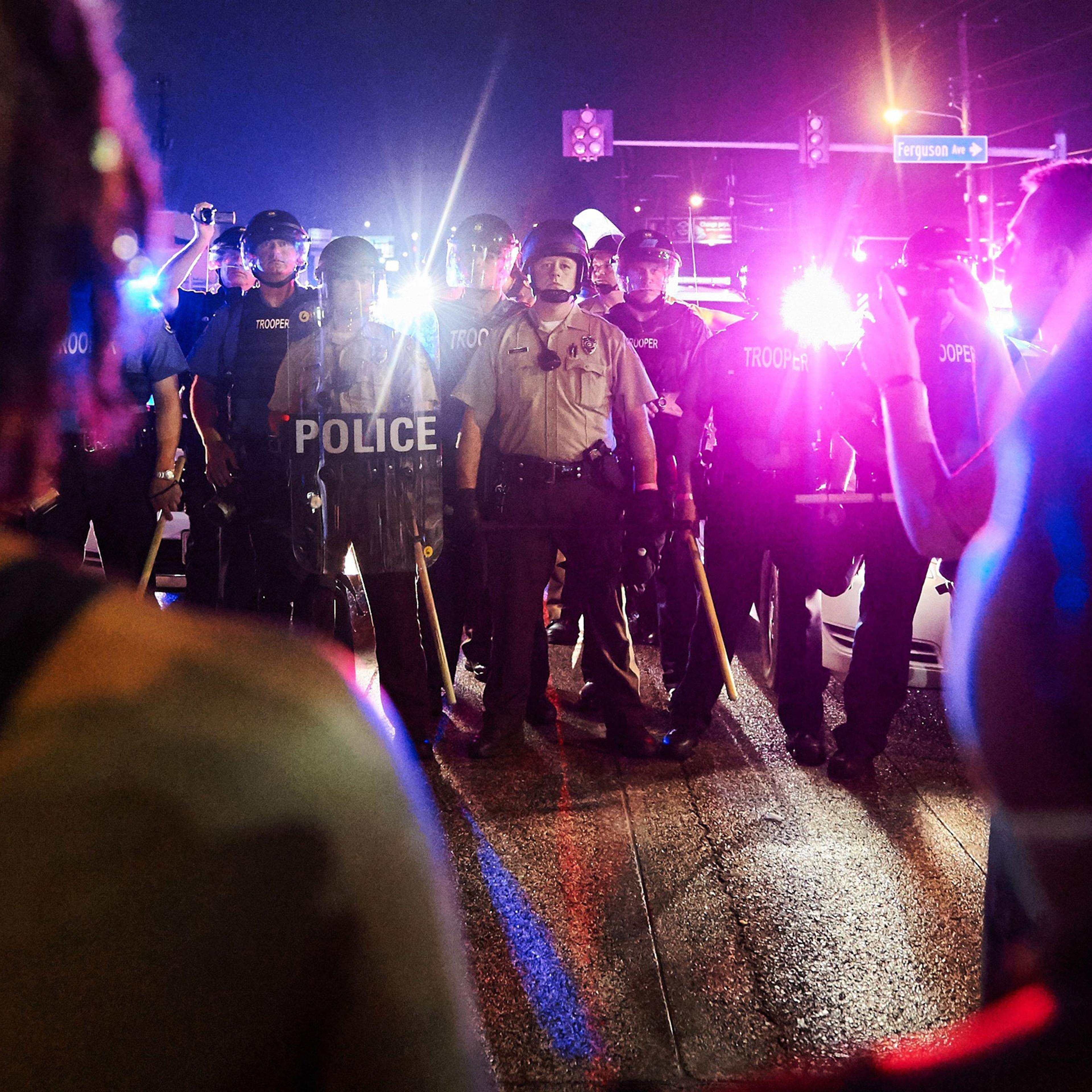 St. Louis County Police and Missouri State Highway Patrol troopers (C) stand guard as protesters (foreground) march on West Florissant Avenue in Ferguson, Missouri on August 9, 2015. A day of peaceful remembrance marking the anniversary of 18-year-old bl